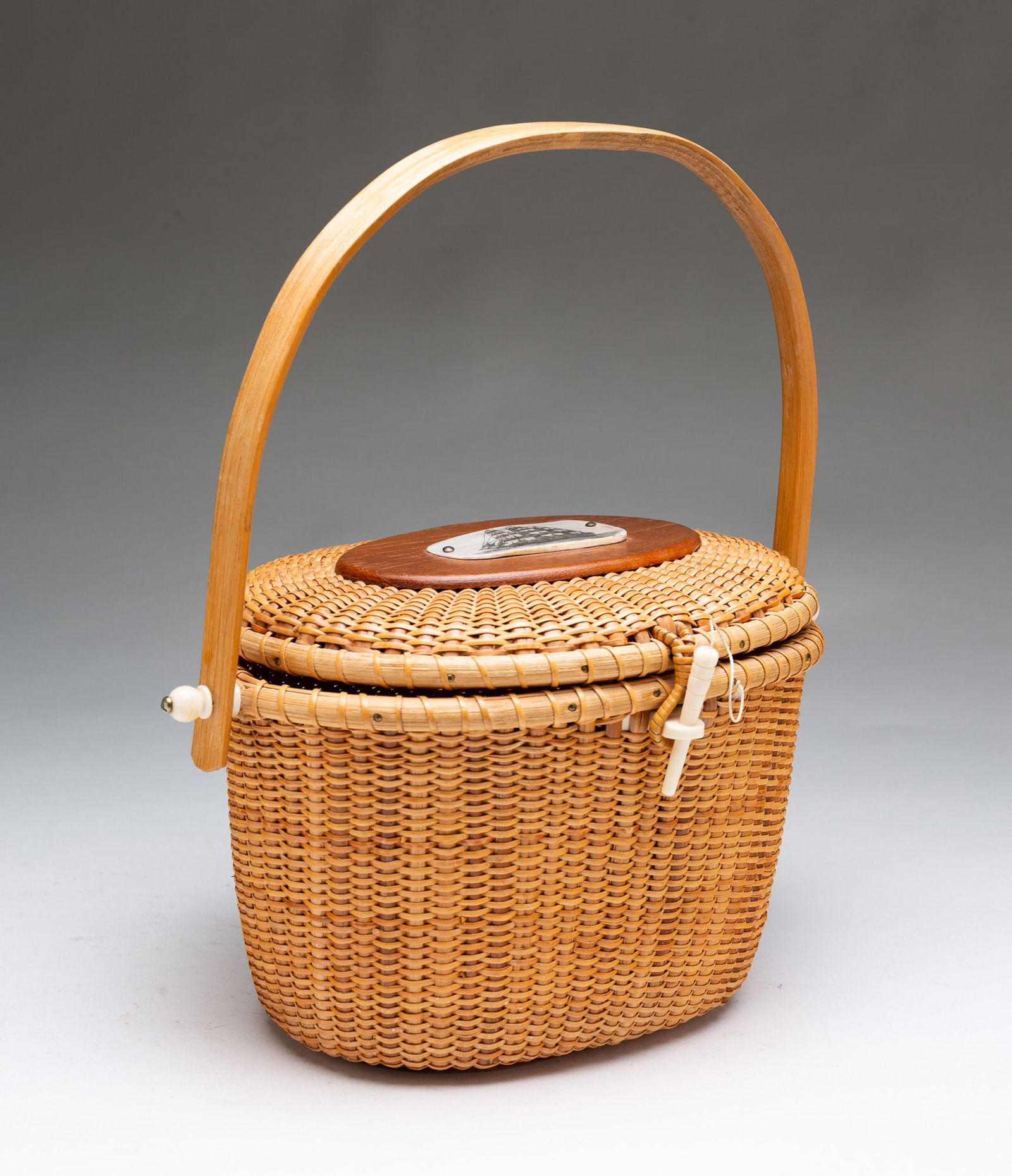 NANTUCKET LIGHTSHIP BASKET PURSE SIGNED D. KRAPF.: American (Massachusetts), 20th Century. Splint woven basket with bentwood handle, hinged lid, engraved scrimshaw plaque signed "D. Krapf" and fastener. 6.5"h. 11.25"w.