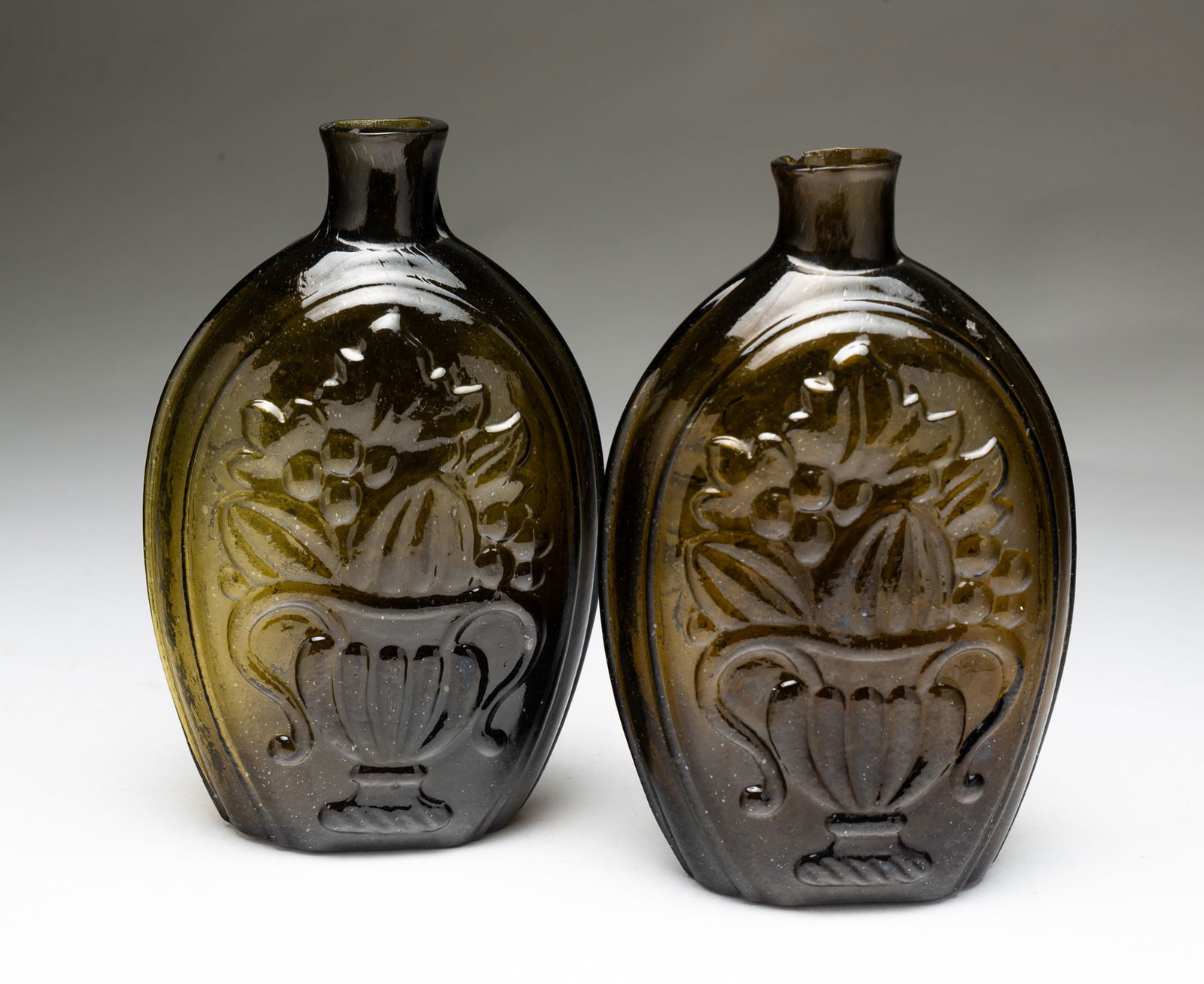 PAIR OF AMERICAN CORNUCOPIA BLOWN FLASKS.: American, First half 19th Century. Olive glass, cornucopia and fruit on one side and urn of fruit on reverse. Broken pontils. 6.75"h.