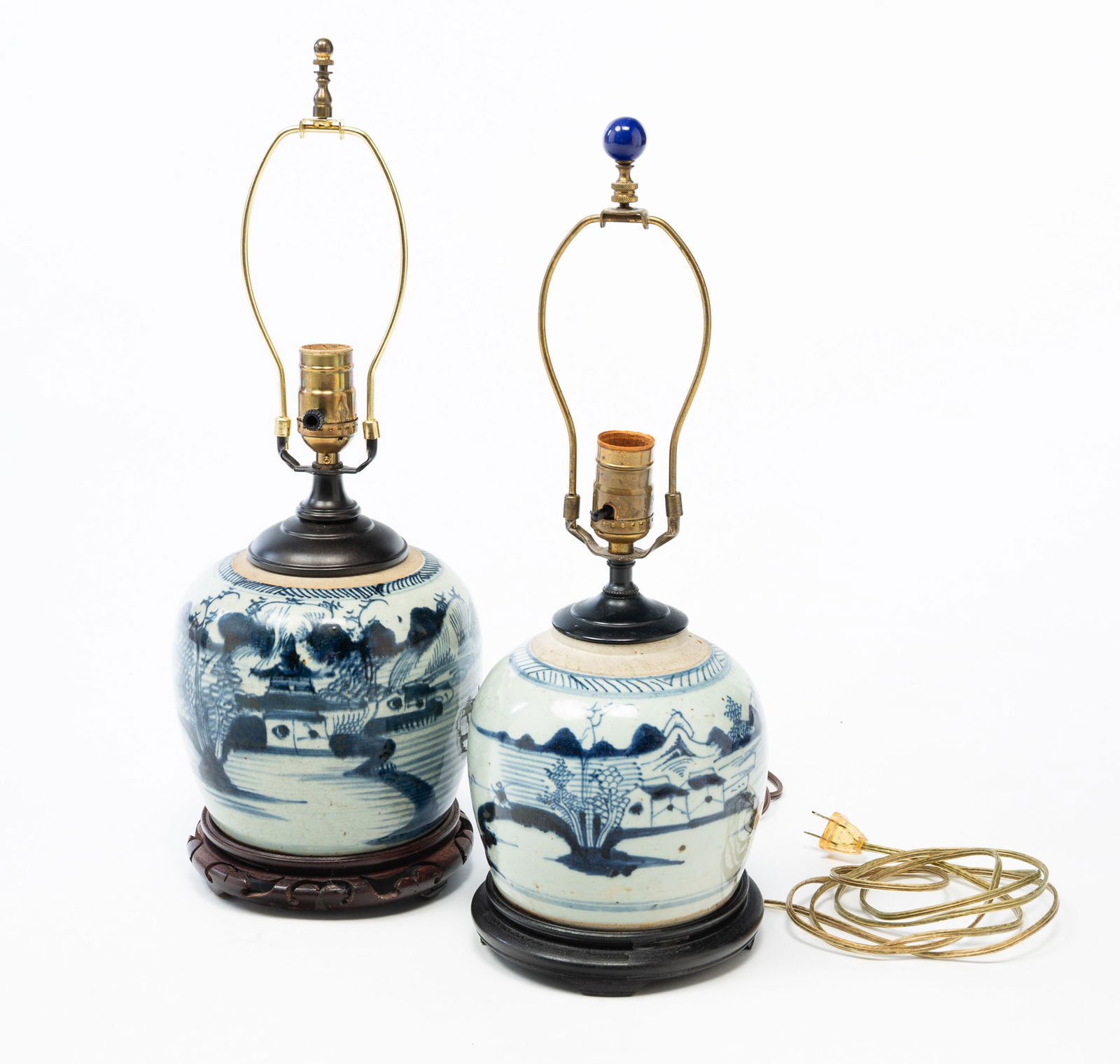TWO CHINESE BLUE AND WHITE CANTON PORCELAIN GINGER JAR LAMPS.: China, ca. 1840. Decorated with scenes of pagodas, mountains, trees, water, and fisherman, both on wooden bases and having harps with finials. Later converted to electric lamps by Gross Electric (Tole