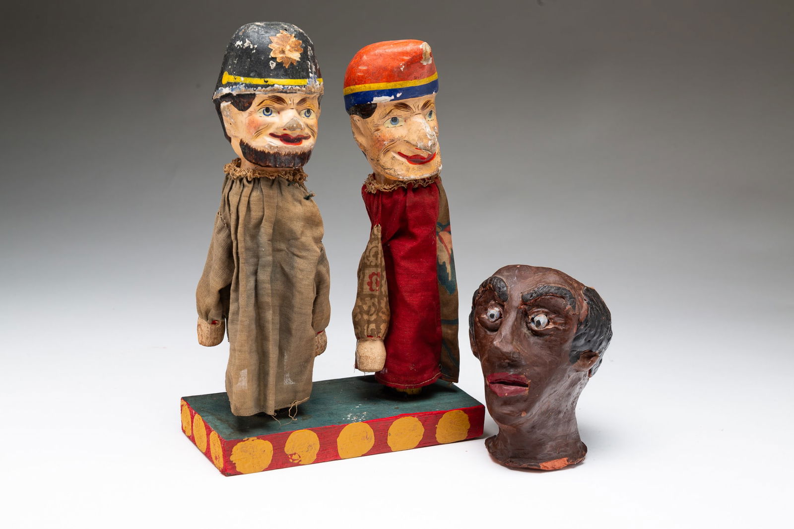 TWO PUPPETS AND A FOLKSY REDWARE BUST OF A MAN.: 20th Century. Puppets with papier-mache heads, wood hands and machine sewn cloth robes, and blue, yellow and red painted stand. 10.25”h. 6.75''w. 3.25"d. Redware bust of a balding gentleman. 4.7