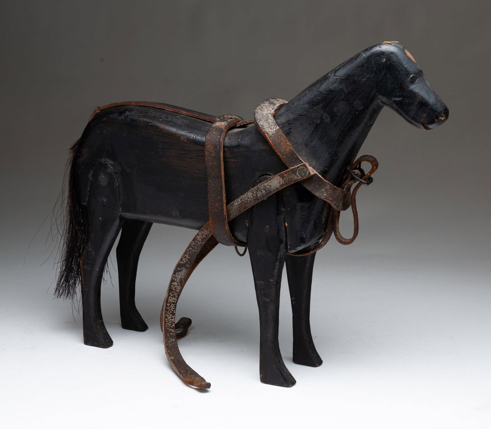 AMERICAN AMISH HORSE TOY.: American, ca. 1900. Pine. Carved body and legs, round nail construction, horse hair tail and leather harness. 12"h. 13"l.Provenance: Ex Missouri Plain Folk (Skeston, Missouri).