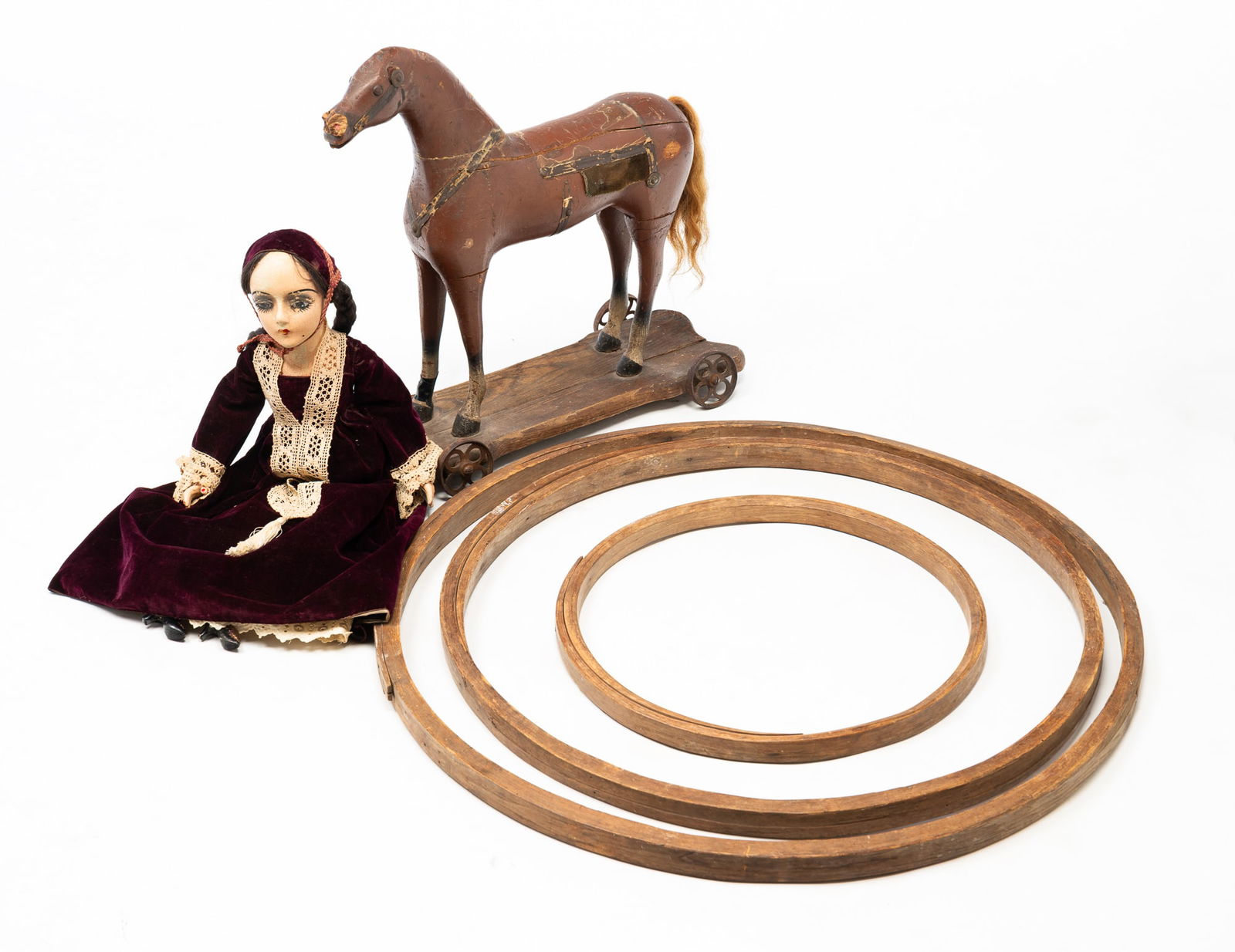 AMERICAN TOY LOT.: American, 19th and 20th Centuries. Three oak hoop toys. 17.75"d. to 31"d. A Converse horse pull toy with label. 21.5"h. 21"l. And a papier-mache female doll with velvet dress and lace trim. 26"h.Prove