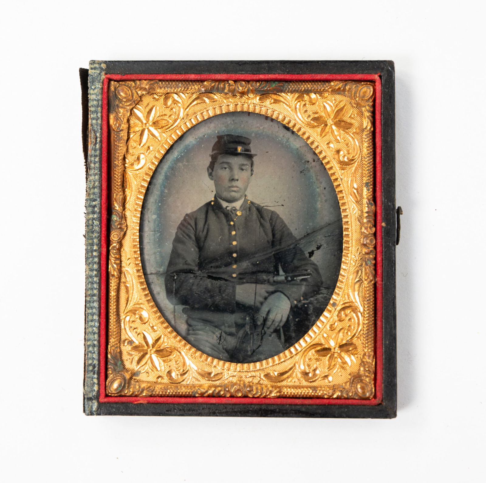 AMERICAN CASED SIXTH-PLATE AMBROTYPE OF CIVIL WAR SOLDIER.: American, 19th Century. Ambrotype. Seated uniformed soldier wearing a kepi and holding an Army Colt revolver. Gold painted highlights. In half of a pressed cardboard case.