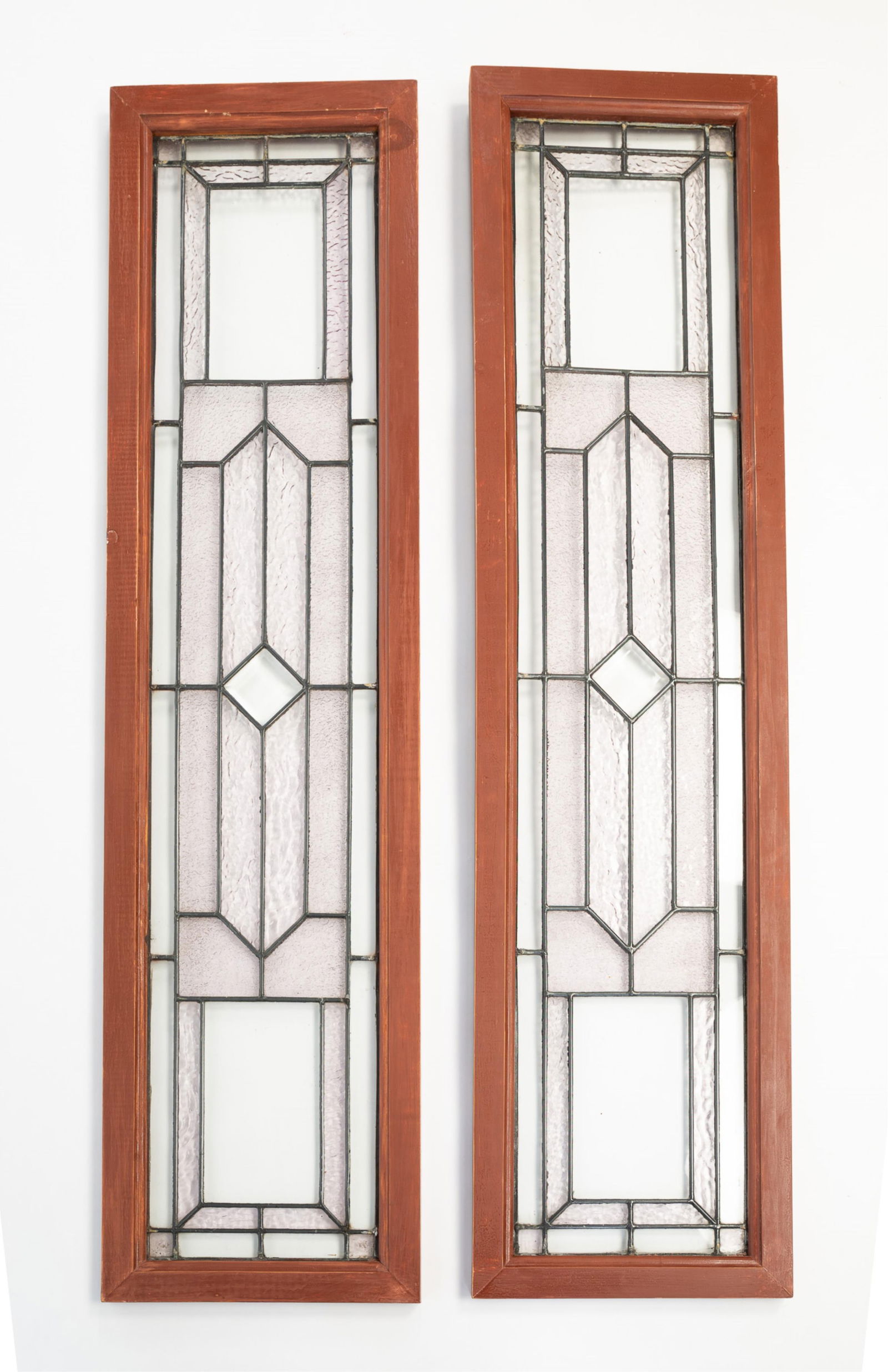 PAIR OF AMERICAN LEADED GLASS WINDOWS.: American, 20th Century. Geometric patterns with some textured glass and center diamond shaped beveled jewel. In painted wooden frames. 51''h. 13''w.Provenance: From the Lifetime Collection of the Late