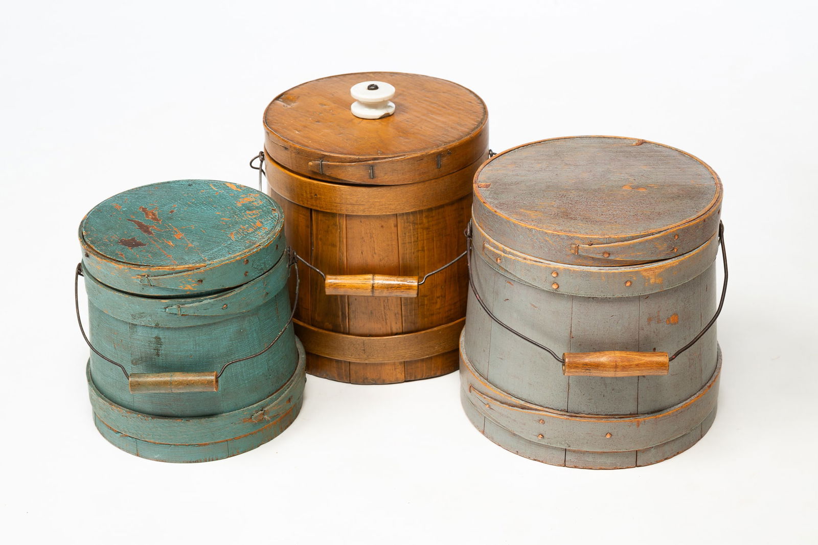 THREE FIRKIN WITH WIRE BALE HANDLES.: American, 19th Century. Pine. Stave construction with oak hoops. One in natural finish with porcelain "BRUNT" knob. 8.5"h. 8"w. at bottom. One in all over gray paint with copper tacks. 7.75"h. 8"w. An