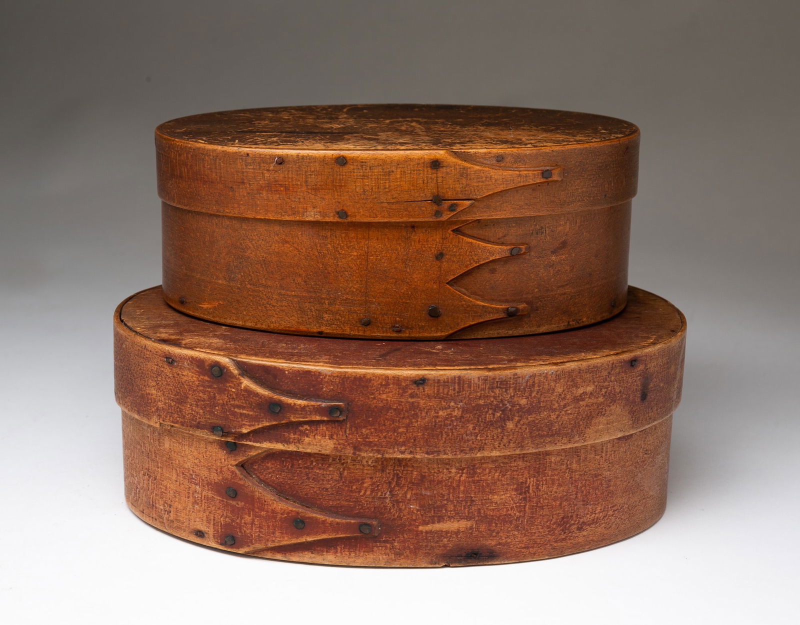 TWO AMERICAN OVAL BENTWOOD PANTRY BOXES.: American, 19th Century. Oval bentwood boxes in graduated sizes with finger joints, pegged construction and copper tacks. Larger with worn red wash, 3.25"h. 9"w. Other with natural finish.