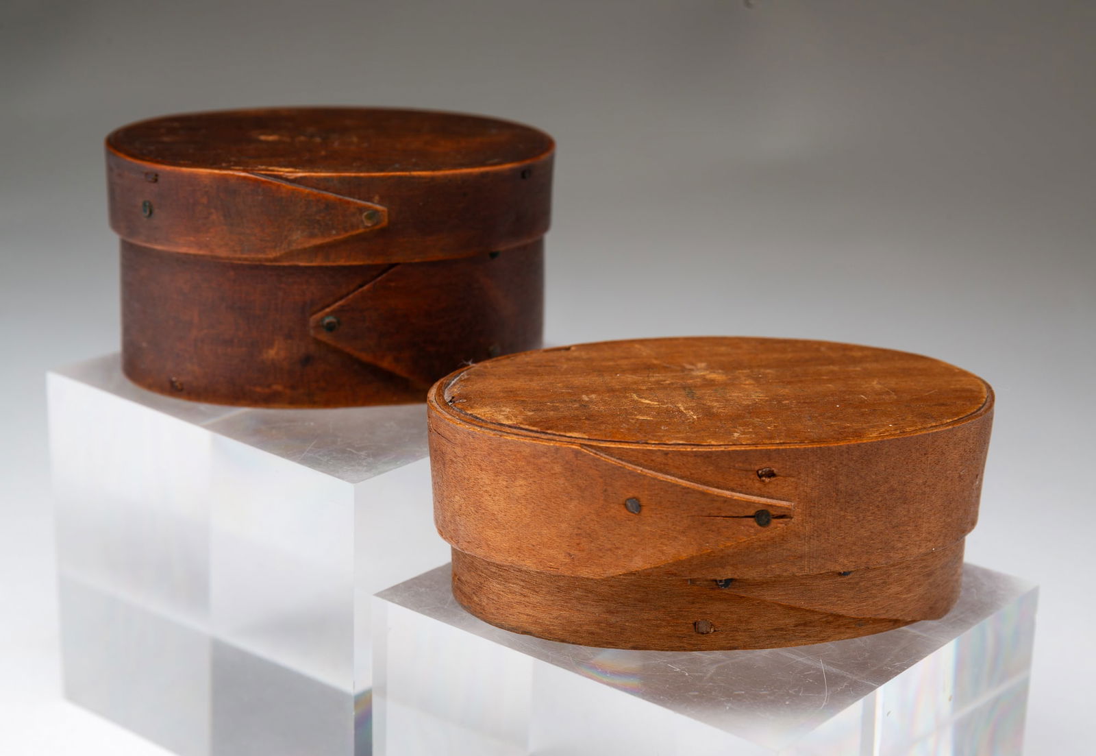 TWO MINIATURE BENTWOOD PANTRY OR SEED BOXES.: American, 19th Century. Oval boxes with pegged construction finger joints and tack decoration. One with dark finish, 1.75"h. 3.1"w. Lighter finish, 1.4"h. 3.6"w.