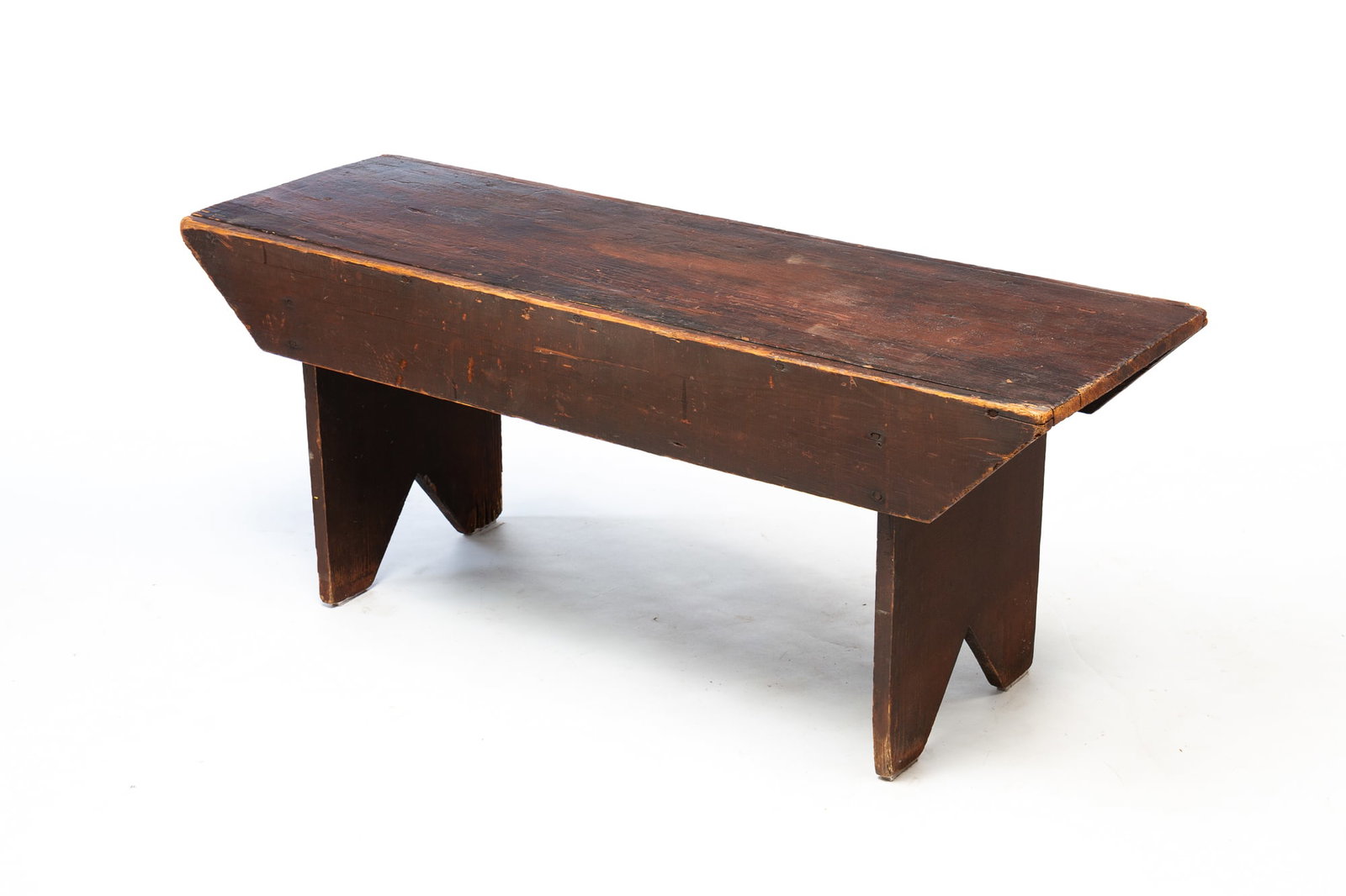 AMERICAN REDDISH-BROWN PAINTED PINE BOOTJACK BENCH.: American, Early 20th Century. Pine. One board top and ends, front and back trapezoidal battens, boot jack ends and worn reddish-brown paint. 19"h. 47"w. 15.5"d.Provenance: From the Lifetime Collection