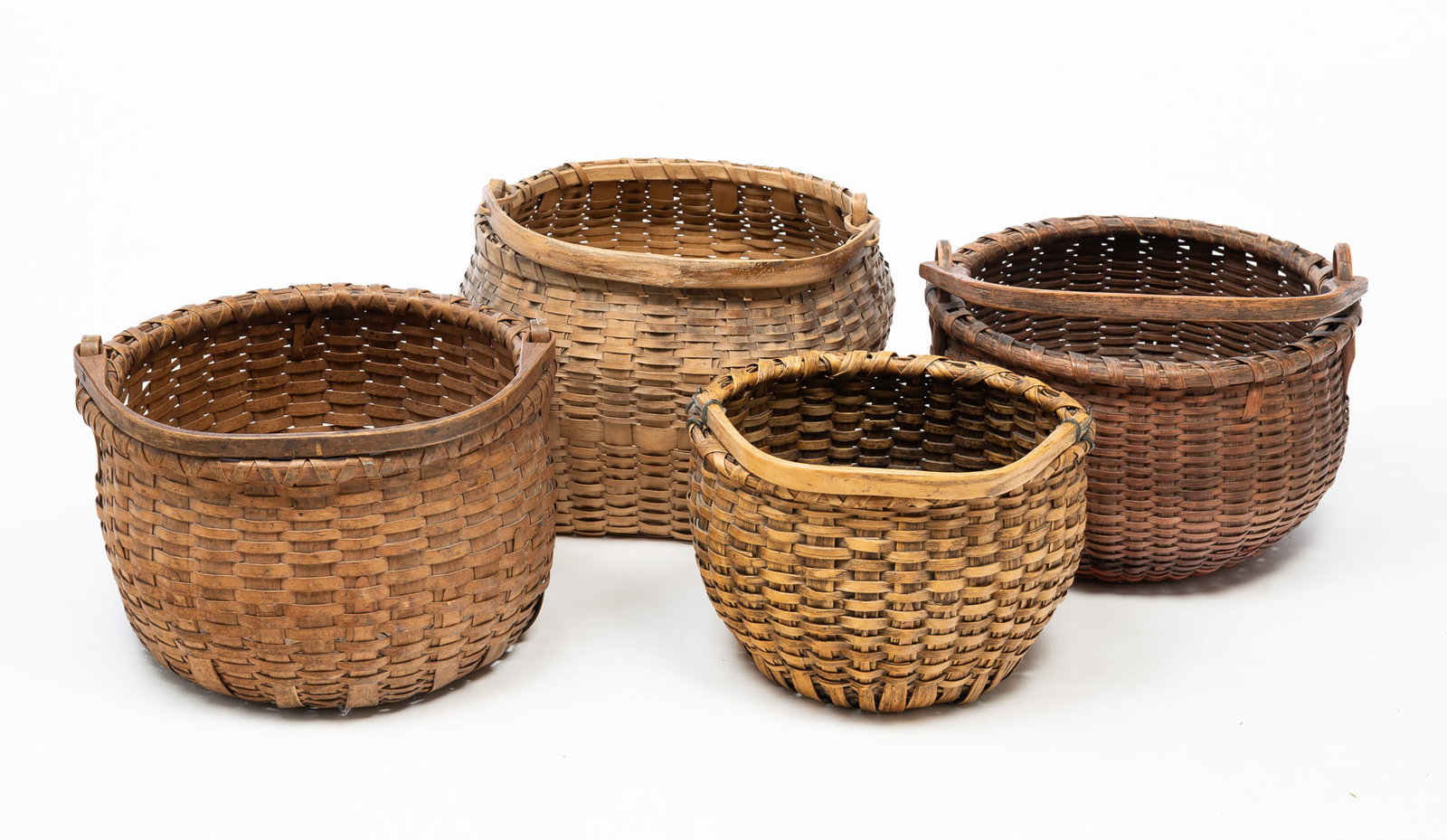 FOUR WOVEN SPLINT SWING HANDLE BASKETS.: American, Late 19th Century. Two round forms, 8.5"h. and 8.75"h., an oval form, 8"h., and one rounded square, 11"h. All with bentwood handles.