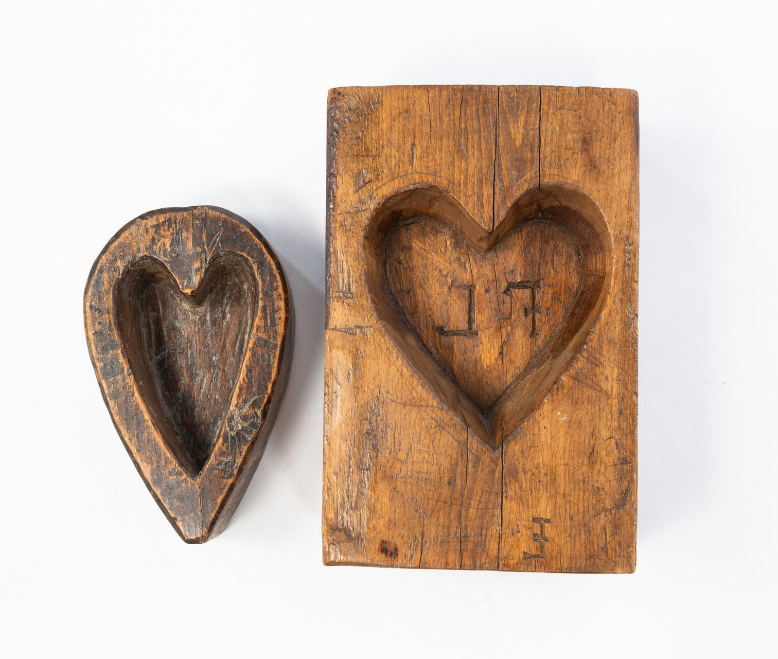 TWO AMERICAN HEART-CARVED MAPLE SUGAR MOLDS.: American, ca. 1900. Mixed woods. Largest with heart and initials "FL" to center. 2.75"h. 4.5"w. 7"l. And a teardrop shaped mold with carved heart, 1.5"h. 3"w. 5"l.