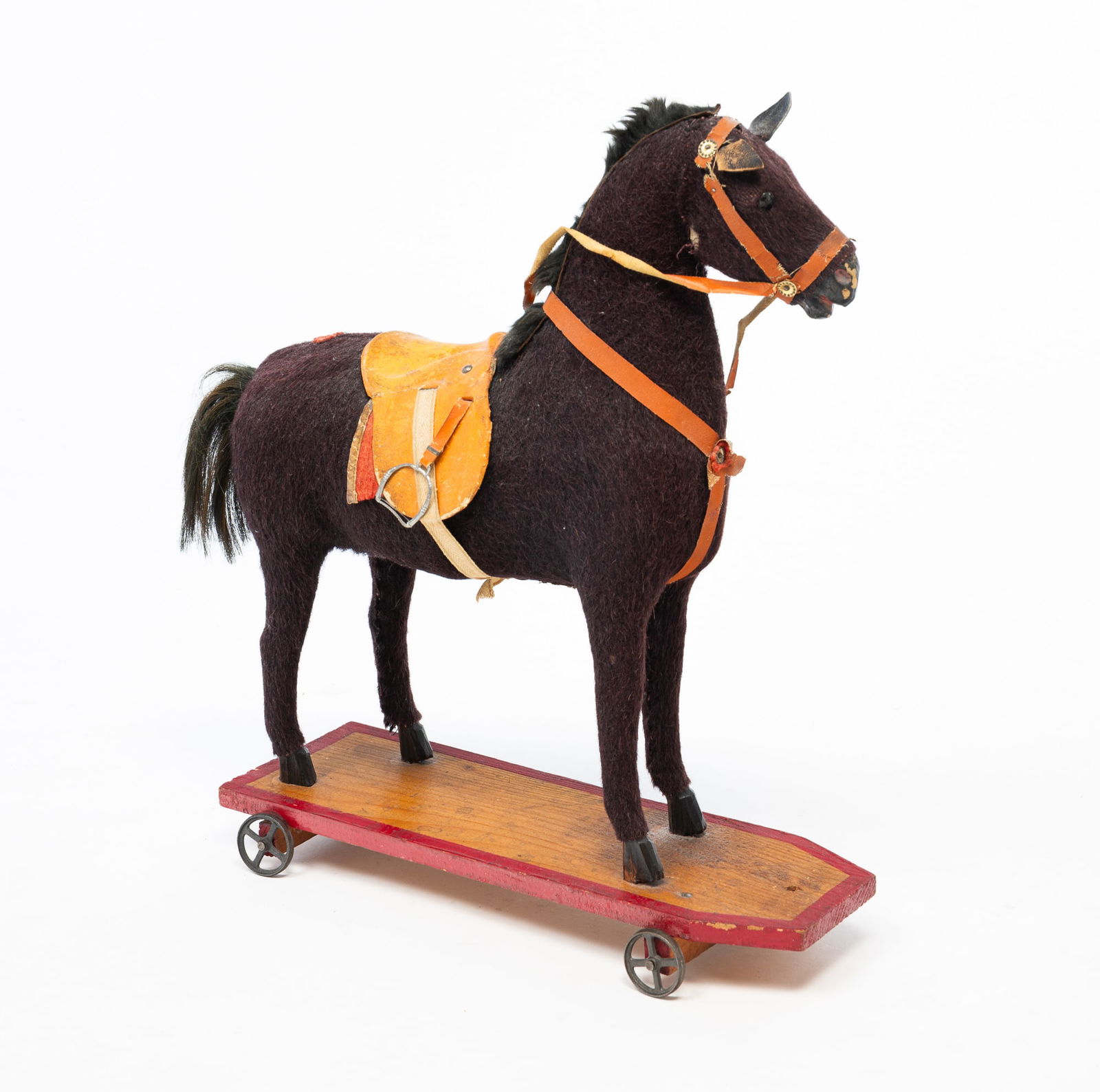 GERMAN MOHAIR-COVERED PAPIER-MACHE HORSE PULL TOY.: Germany, Early 20th Century. Papier-mache body covered in black mohair, wooden legs, glass eyes, leather ears, leather reins, an fur mane and horsehair tail, mounted on a shaped wooden base with red p