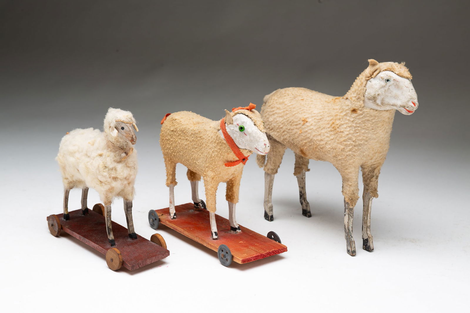 THREE SHEEP TOYS.: German, ca. 1900. A plaster sheep toy with woolen coat and wooden legs, 7"h. 7"l. And two sheep pull toys. A wooden sheep with wooly coat on platform base with wooden wheels. 5.5"h. 2.25"w. 5.75"l. An