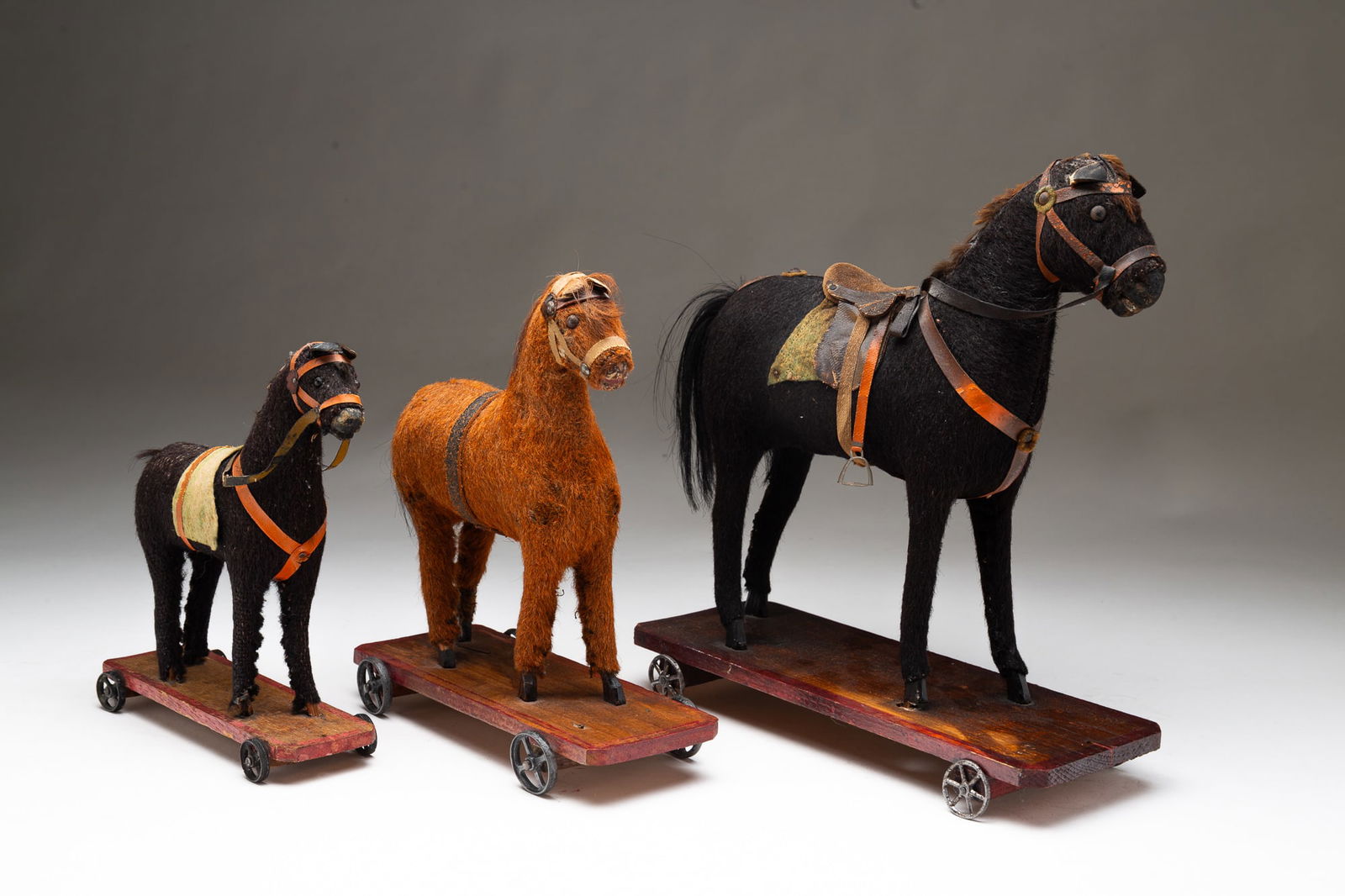 THREE GERMAN HORSE PULL TOYS.: Germany, Early 20th Century.Largest with brown mohair coat, horsehair tail, and fur mane, on a dark stained base with iron wheels. 11.25"h. 4"w. 10.5"l. Middle with reddish mohair coat, fur mane and h