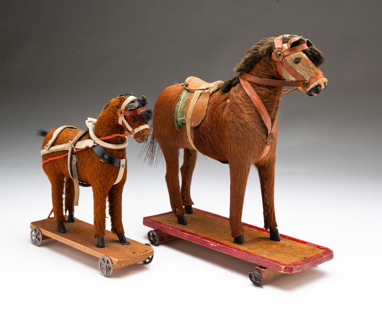 TWO GERMAN HORSE PULL TOYS.: Germany, ca. 1900. Deerskin coat, horsehair tail, and fur mane, on a painted wood base with iron wheels. 10.5"h. 3.75"w. 9.5"l. And the second with mohair coat, horsehair tail, on a pine base with red