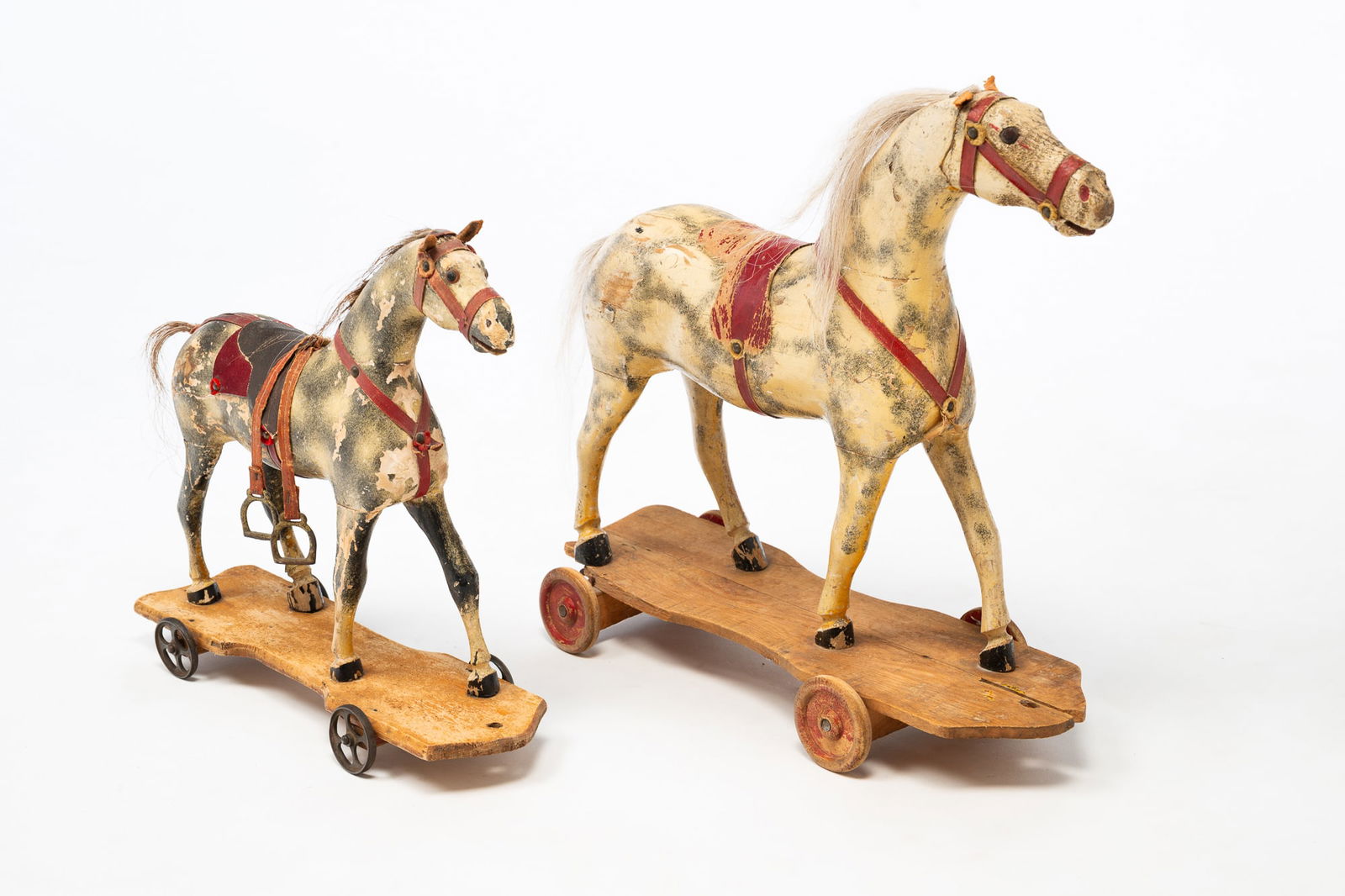TWO GERMAN CARVED AND PAINTED PINE HORSE PULL TOYS.: German, Late 19th Century. Pine. Multi-section horses with white and gray dappling, horsehair manes and tails, metal eyes, and leather ears. Shaped bases with four wheels. Larger on base with wooden w