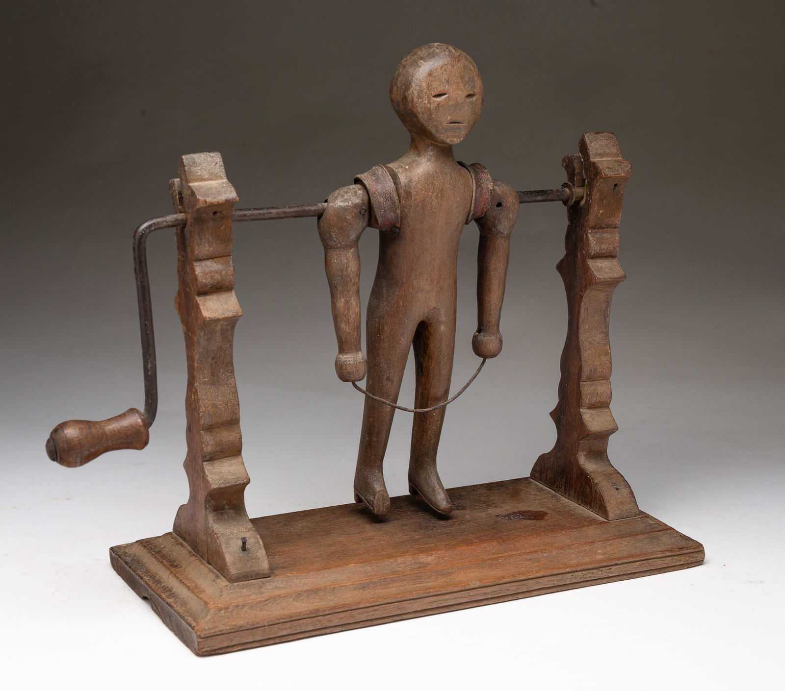 AMERICAN FOLK ART CARVED WALNUT CRANK-ACTION JUMP ROPING FIGURE.: American, 19th Century. Walnut. Crank action figure with leather accents mounted on a platform base with ornate carved posts. 9.5"h. 11.5"w. 5.5"d.Provenance: From the Lifetime Collection of Chuck Aue