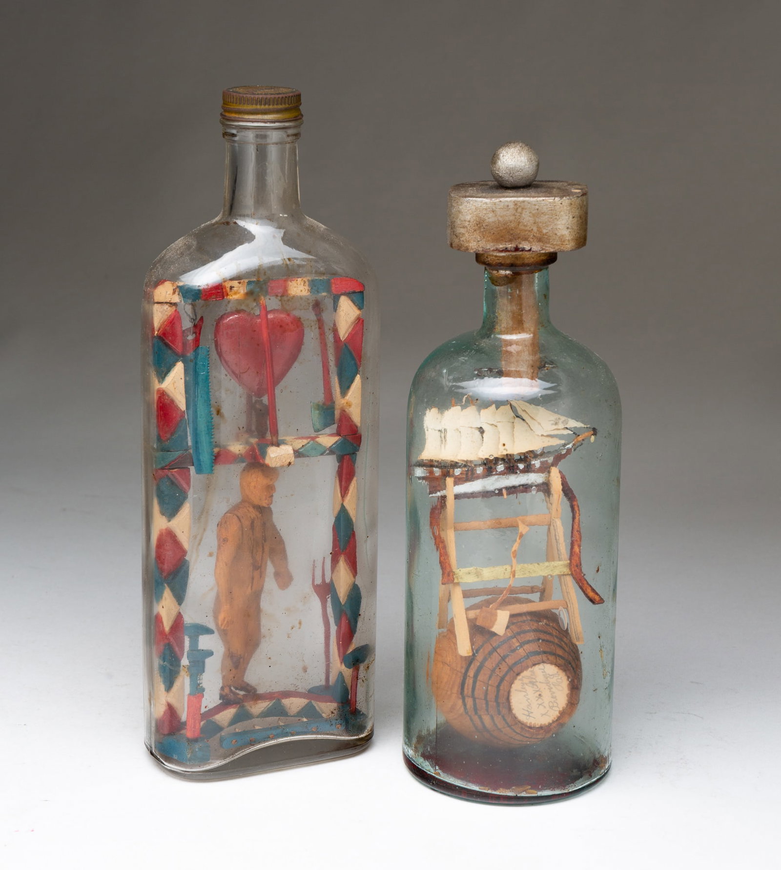 TWO AMERICAN FOLK ART BOTTLE WHIMSEYS.: American, 20th Century. The first containing a miniature carved and painted tall masted ship on a saw horse sitting on a barrel signed "Hanleyz XXXX Ales Providence R.I." on one side "Frank James Gold