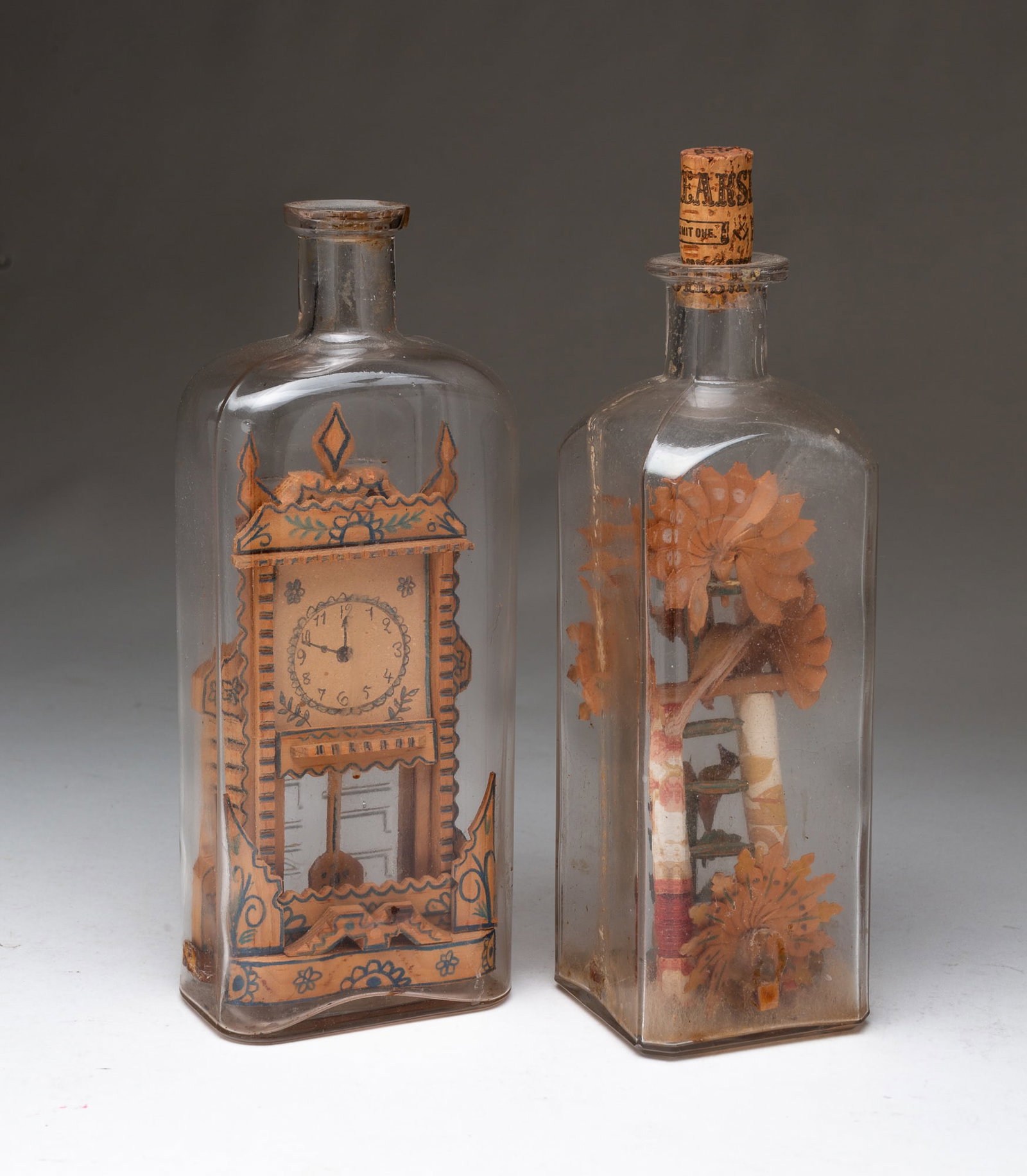 TWO AMERICAN FOLK ART BOTTLE WHIMSEYS.: American, 20th Century. The first containing miniature carved and painted wood peacock feathers and birds, the other containing a carved and painted wood tall clock. Taller bottle (with cork stopper),