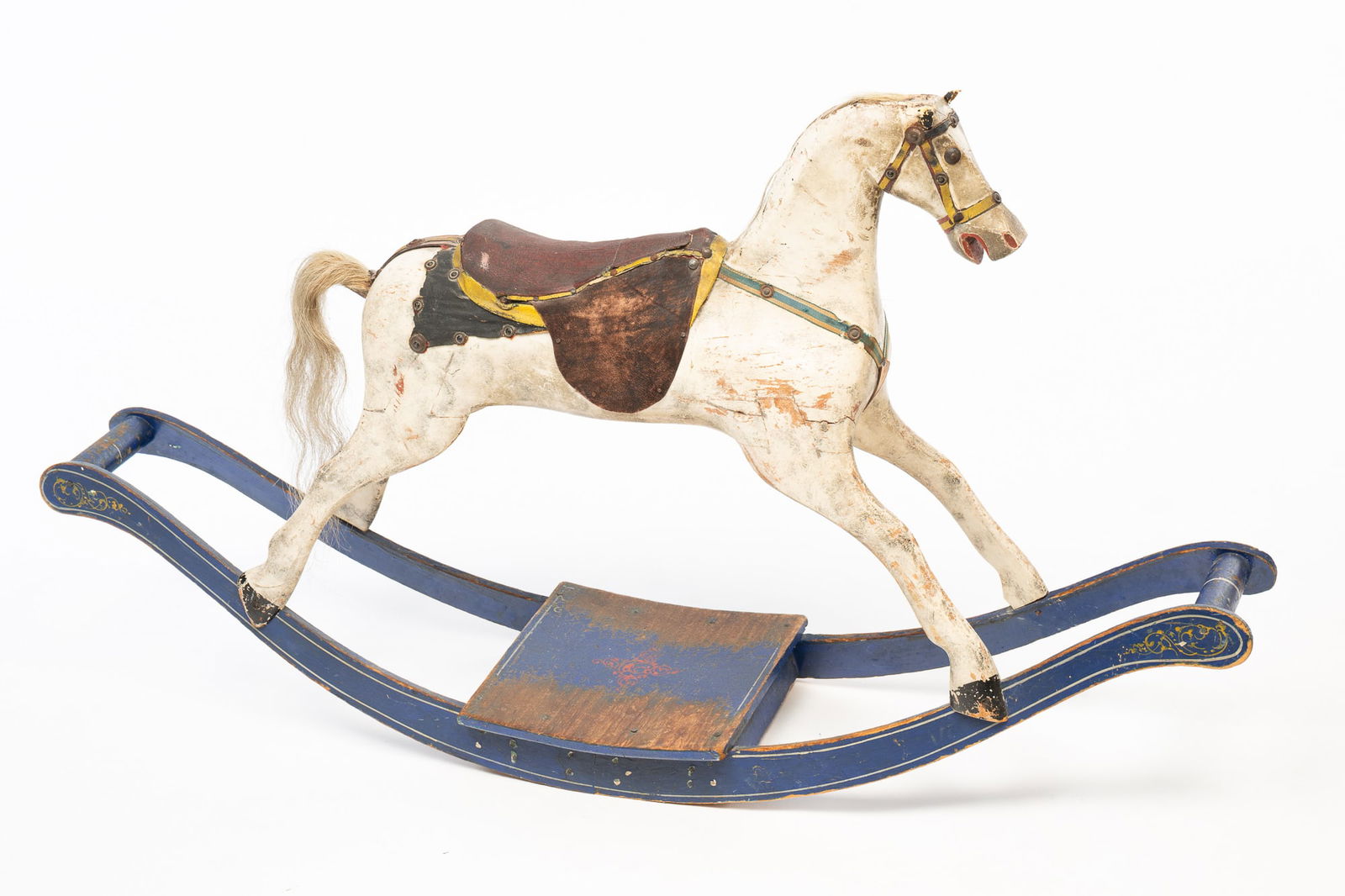 AMERICAN CARVED AND PAINTED WOOD ROCKING HORSE.: American, Early 20th Century. Pine. Multi-section horse with white paint, horse hair tail and mane, rivet eyes, leather ears, red leather saddle with seat and trim and painted decoration. Base with bl