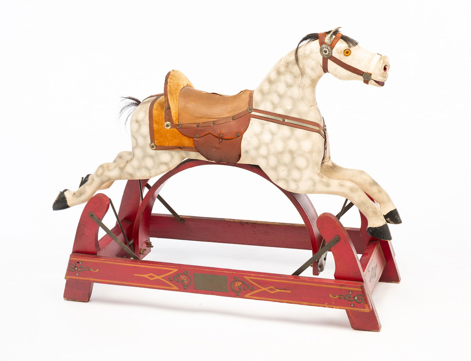 AMERICAN CARVED AND PAINTED WOOD ROCKING HORSE ON GLIDER BASE.: American, Early 20th Century. Pine. Multi-section horse with white and gray dappling, horse hair mane and tail, glass eyes, leather ears, leather harness, reins and saddle with chenille trim, corduroy