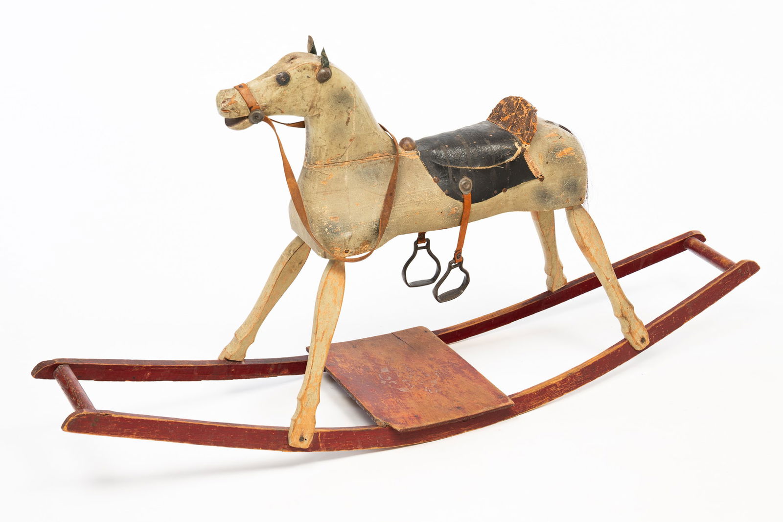 AMERICAN CARVED AND PAINTED WOOD ROCKING HORSE.: American, Early 20th Century. Pine. Multi-section horse with gray paint, horse hair tail, rivet eyes, leather ears, black leather saddle with seat and trim, leather strapped stirrups and rein. Base wi