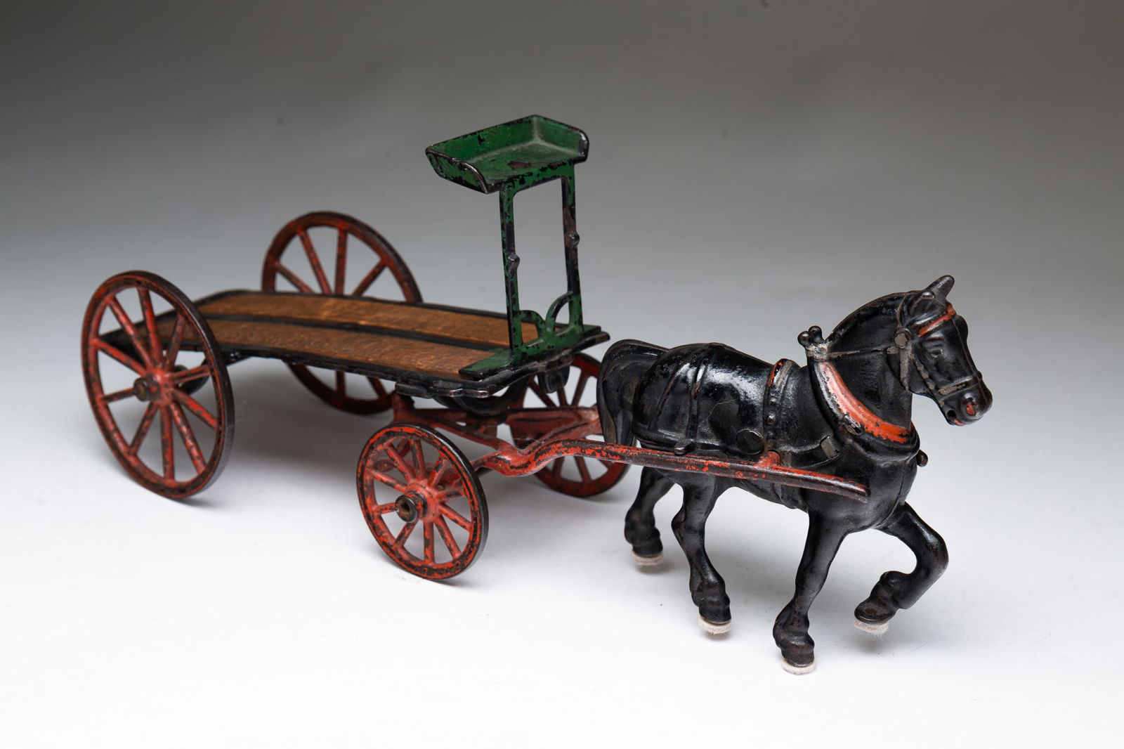 CAST IRON HORSE AND CART TOY.: American, ca. 1900. Cast iron. Black painted horse pulling a iron framed, wood bed cart. 5.5"h. 14"l.