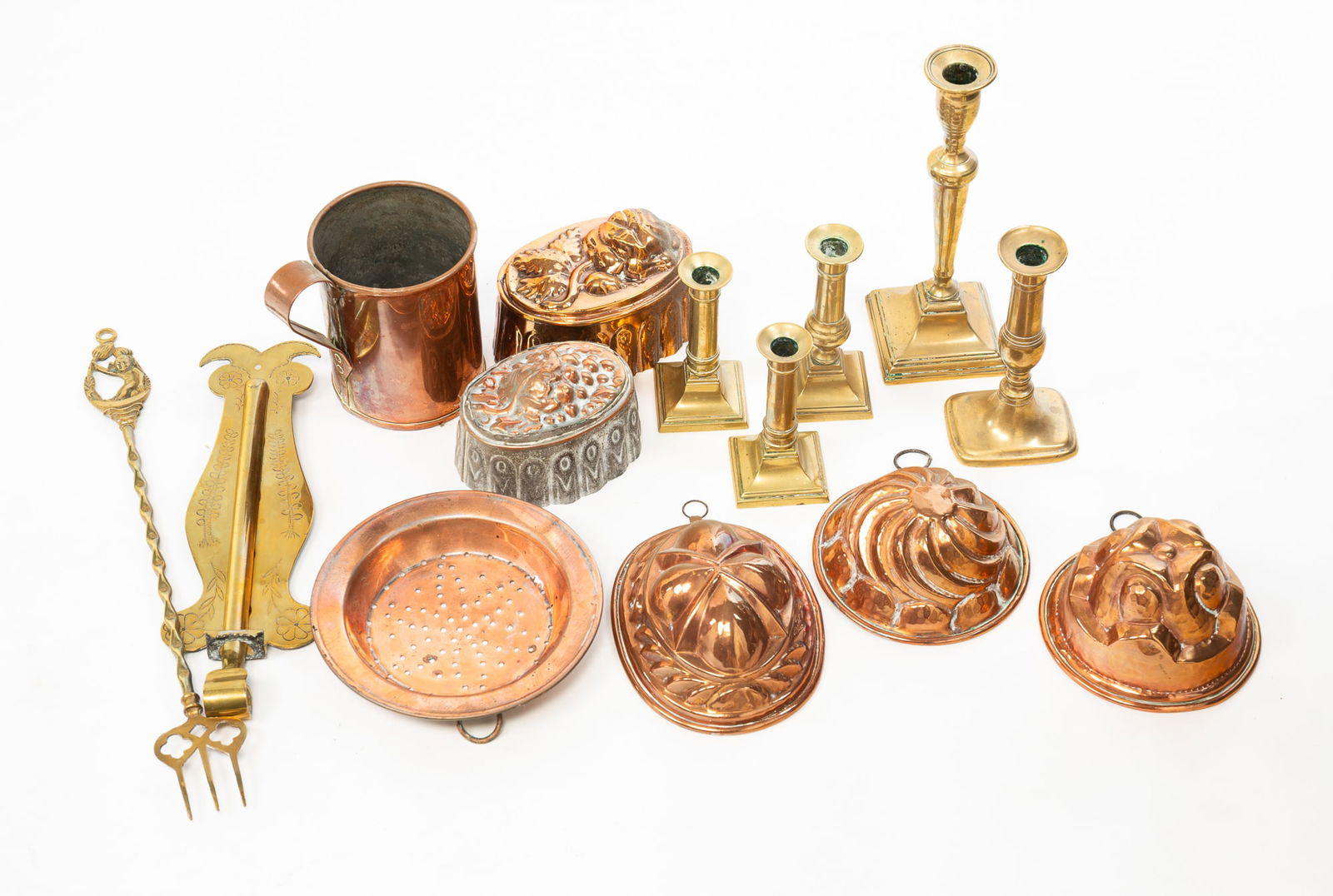 GROUP OF COPPER AND BRASS ITEMS, INCL. CANDLESTICKS AND FOOD MOLDS.: England, 19th-Early 20th Century. Including five copper food molds in various forms, a copper measure, a copper washed strainer, a brass hanging trammel with engraved decoration, 13.75"h., a brass toa