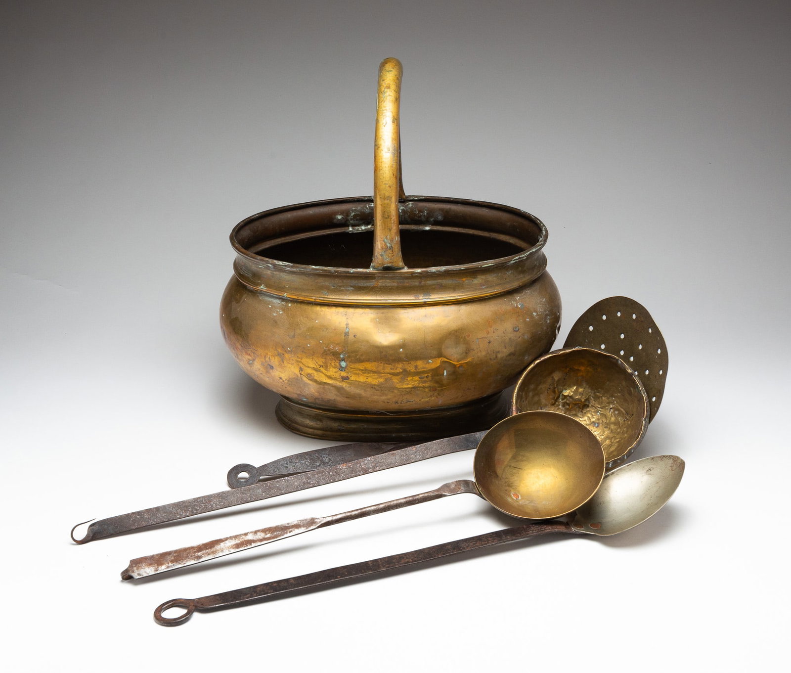 BRASS BUCKET AND FOUR HEARTH SIDE COOKING UTENSILS.: American, 19th Century. A oval shaped brass bucket with handle, 16.5"h. 14.5"w. And four iron and brass utensils including spoons, skimmer and two ladles.