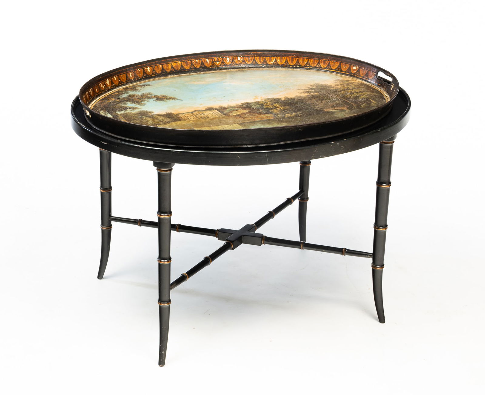 FRENCH SCENIC TOLE-PAINTED TRAY TABLE.: A 19th Century oval tray with cut out handles, country manor with lake and fisherman scene and decorative border. 2"h. 28"w. 21"d. On a 20th Century slightly oversized stand with black lacquer finish,