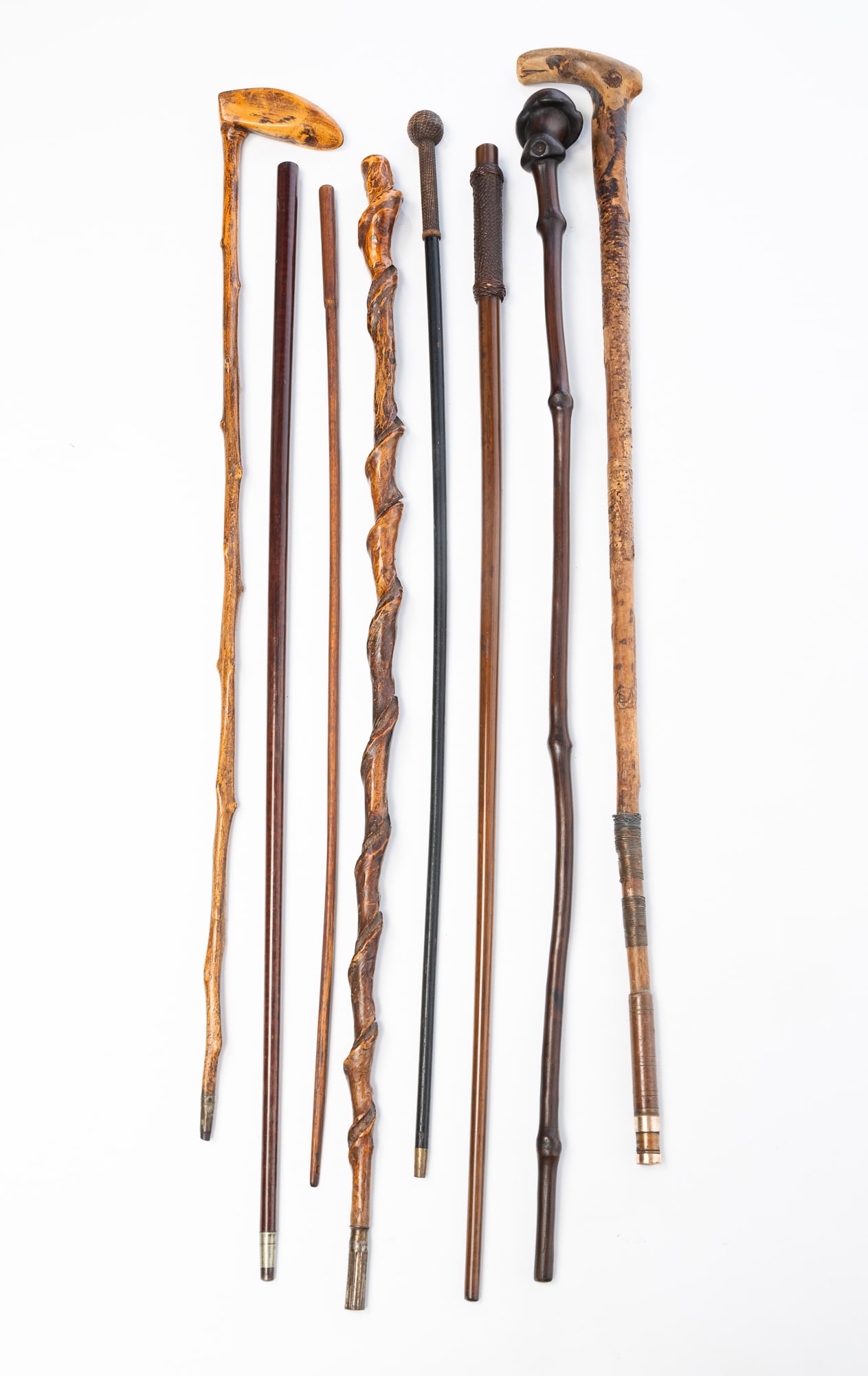 COLLECTION OF CANES AND WALKING STICKS PLUS RIDING CROP.: Late 19th-20th Century. Wood, bamboo, and metal. Comprising two canes and five walking sticks plus a riding crop. Featuring a folksy twist-carved example. Also included are two walking sticks with wov