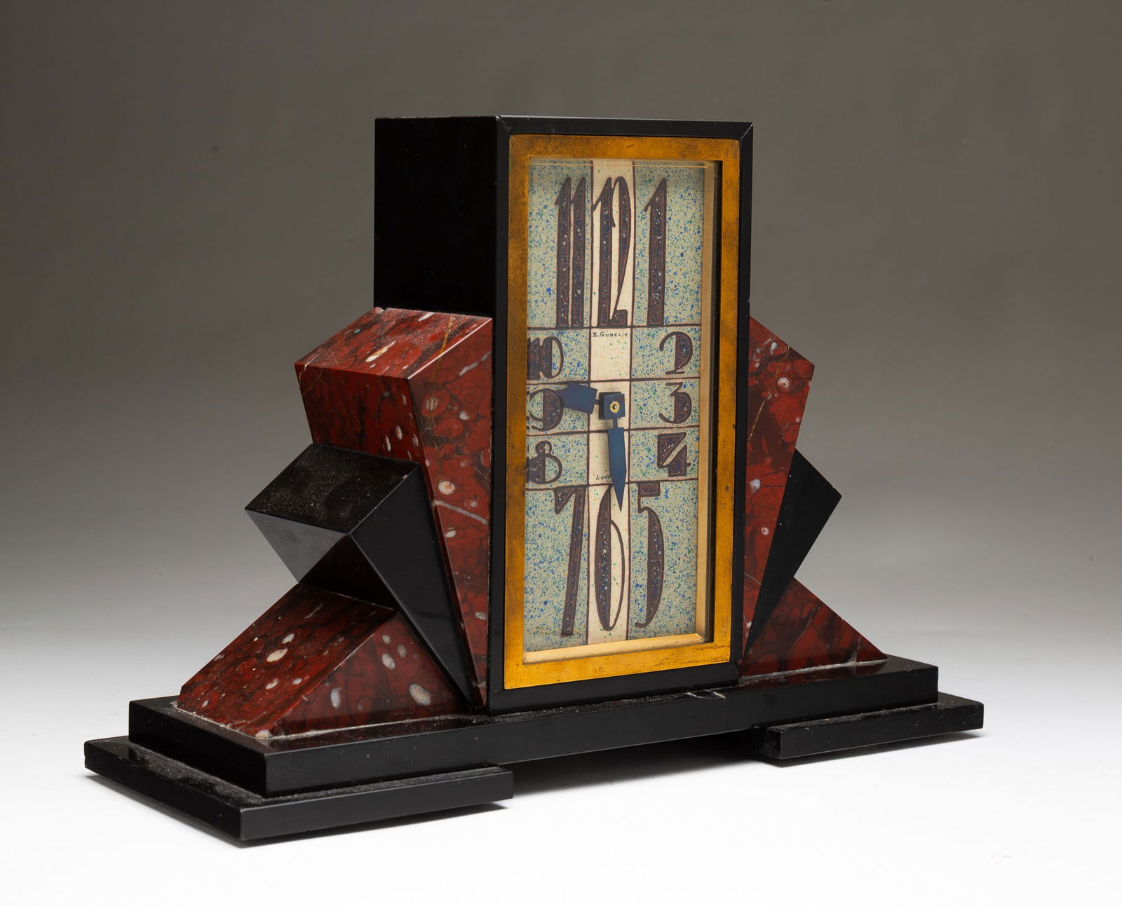GÜBELIN (LUCERNE, SWITZERLAND) ART DECO MARBLE MANTEL CLOCK.: Switzerland (Lucerne), ca. 1920. Mottled light blue and white enamel face with brown Arabic numerals signed "E. Gübelin Lucerne," brass bezel, geometric black stone and red marble case on stepped bla