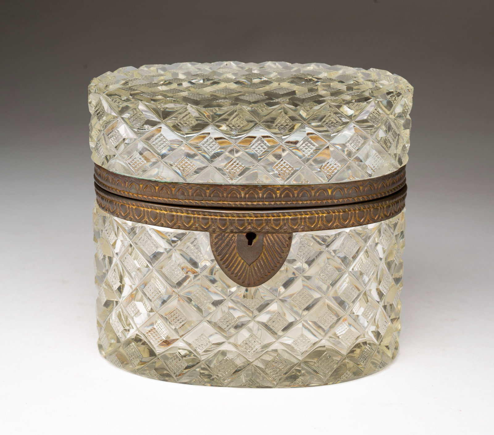 FRENCH BRASS-MOUNTED CRYSTAL JEWELRY CASKET.: French, ca. 1900. Oval form in quilted pattern cut glass with brass trim on escutcheon. With key. 5"h. 5.5"w.