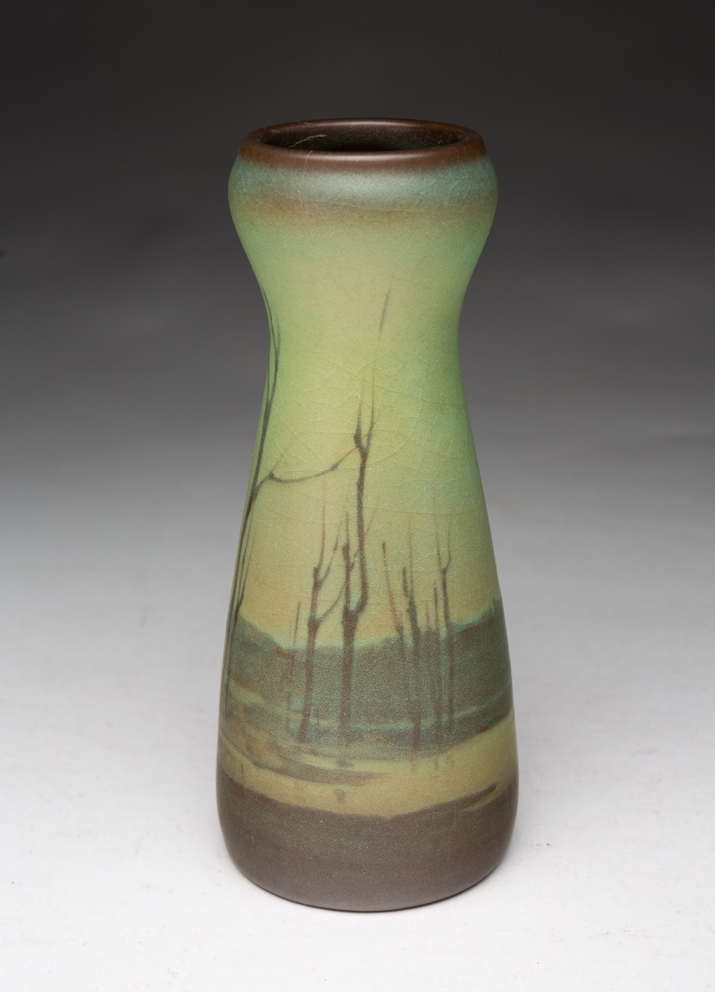 ROOKWOOD POTTERY CO. (CINCINNATI, OHIO) SCENIC VELLUM GLAZED VASE, DATED 1911.: Rookwood Pottery Company (Cincinnati, Ohio), dated 1911. Cylindrical pinched form decorated with barren trees in a green motif. 7.5"h. 3.75"d.