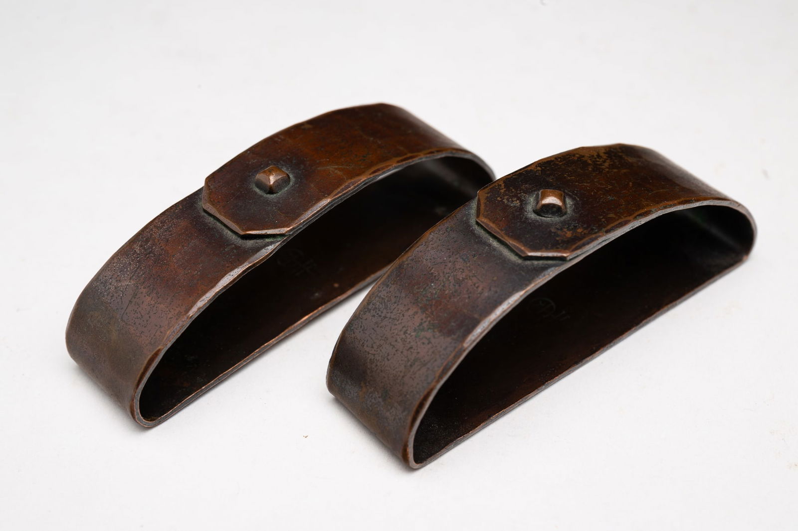 PAIR OF ROYCROFT (EAST AURORA, NEW YORK) ARTS AND CRAFTS HAMMERED COPPER NAPKIN RINGS.: Roycroft (East Aurora, New York), Early 20th Century. Hammered copper napkin rings in original patina. Signed to bottom. 1"h. 2.75"w.