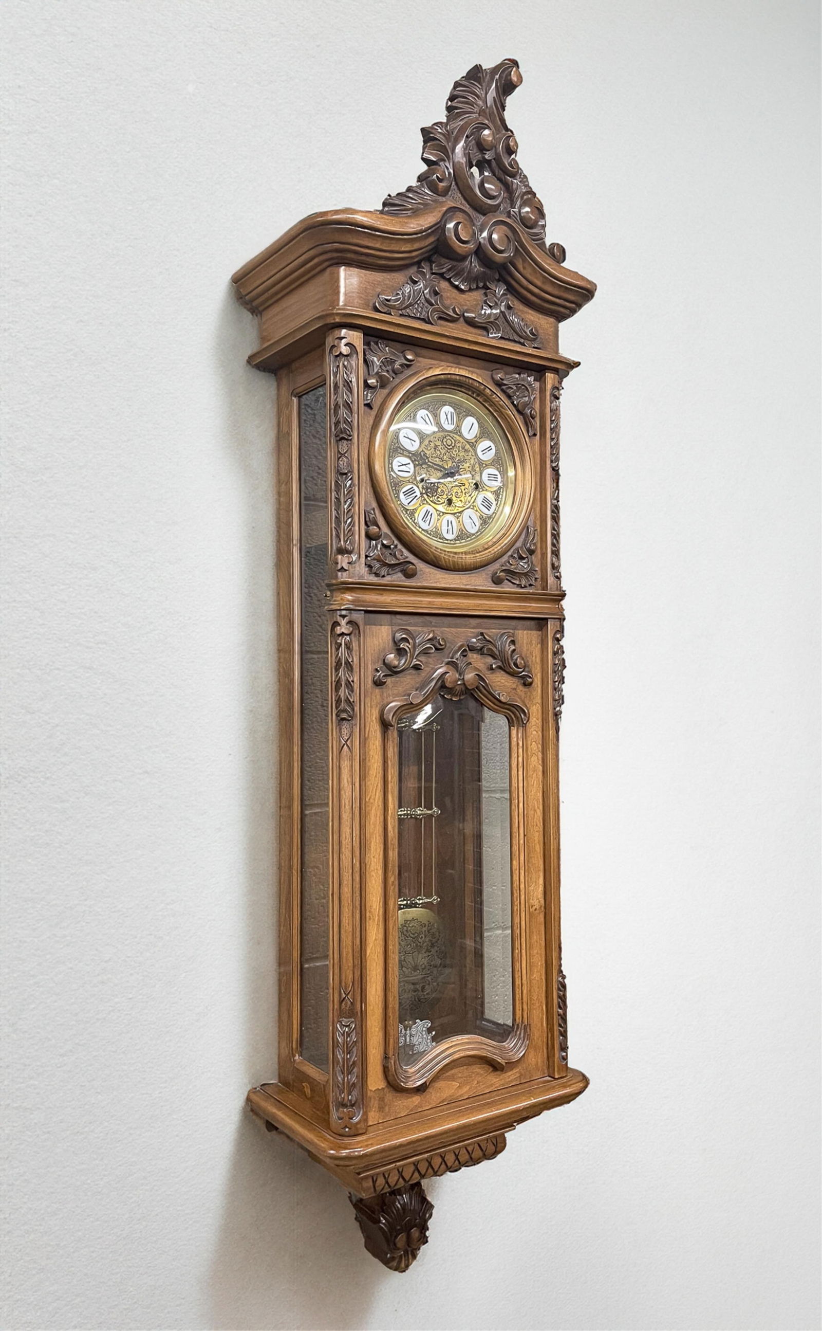 THE GAZO FAMILY CLOCK CO. (SAN DIEGO, CALIFORNIA) CARVED WALNUT WALL CLOCK WITH SEVENTY-TWO NOTE: The Gazo Family Clock Co. (San Diego, California), Late 20th Century. Walnut. Ornately carved case, glass and beveled glass panels, brass and enameled face, brass works and pendulum. 59"h. 17"w. 10"d.