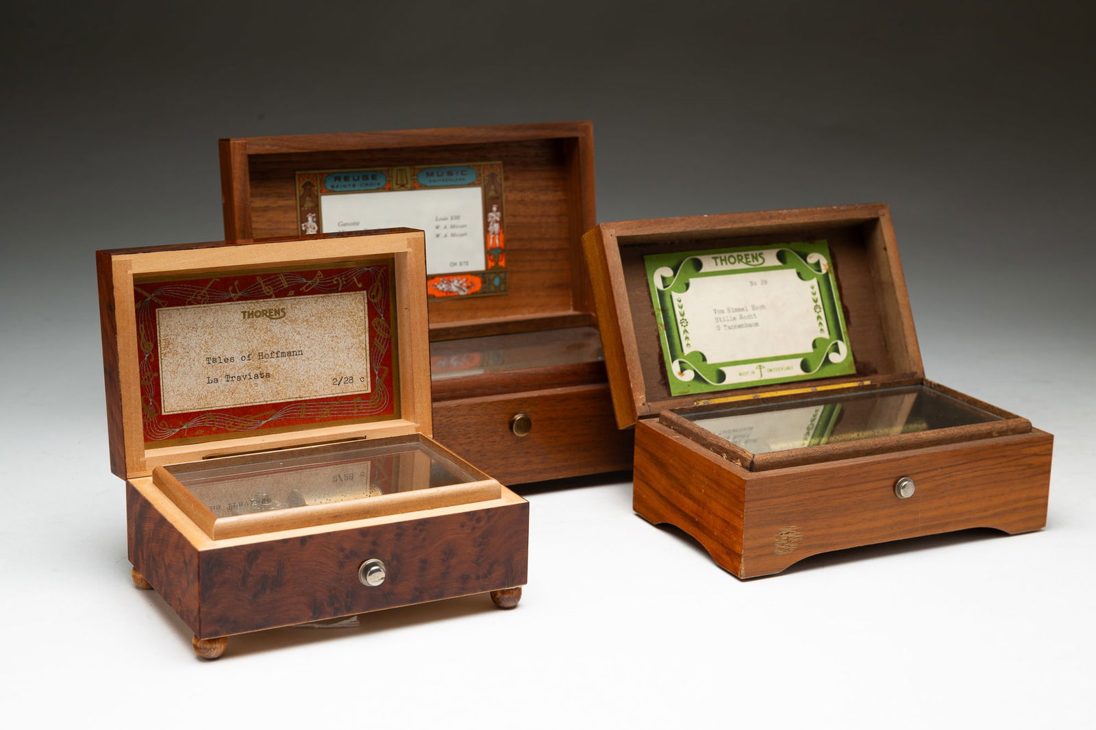 THREE SWISS MUSIC BOXES, INCL. THORENS AND REUGE.: Swiss, 20th Century. A Reuge seventy-two note three-tune box in walnut. 3"h. 8"w. 4.5"d. A Thorens fifty-six note three-tune in a walnut box with inlaid shield on lid. 2.75"h. 6.5"w. 3.75"d. And a Tho