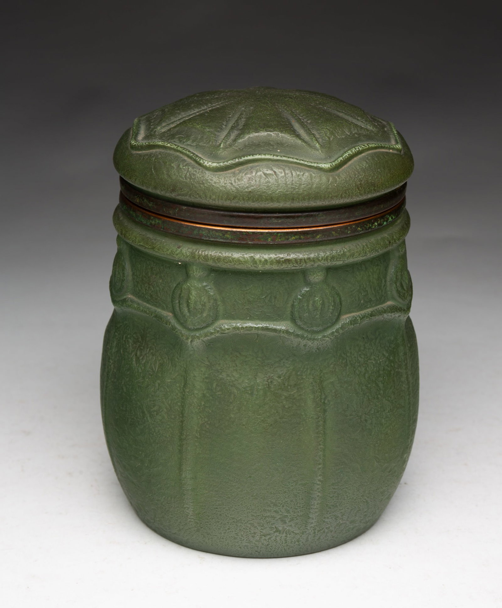 HANDEL (MERIDEN, CONNECTICUT) ARTS AND CRAFTS BRONZE-MOUNTED HUMIDOR.: Handel (Meriden, Connecticut), Early 20th Century. Coated glass and bronze. Cylindrical form, hinged lid humidor with raised pattern design and in a green glaze. Signed to bottom. 6.5"h. 5.75"d.