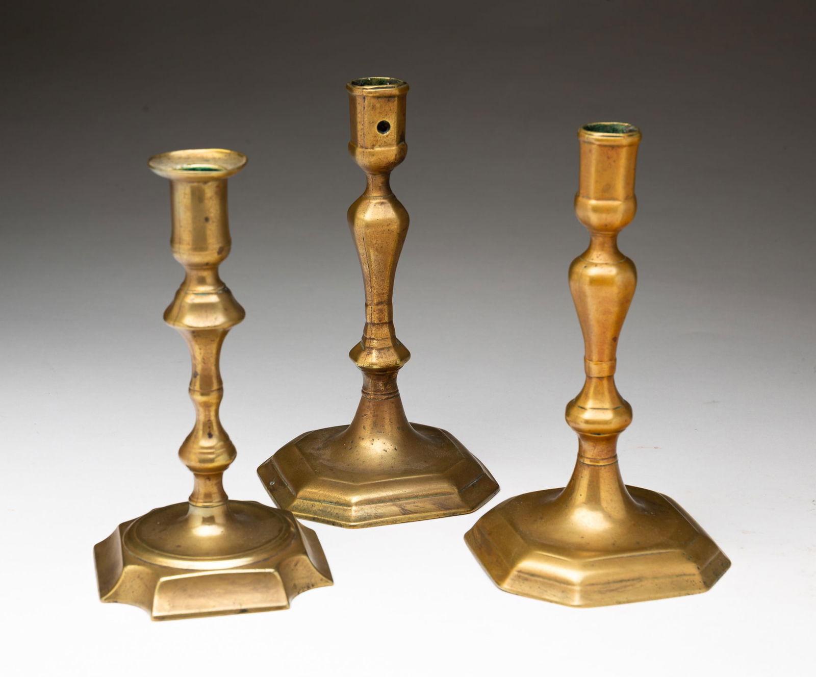 THREE ENGLISH BRASS CANDLESTICKS.: England, 18th Century. Two with faceted baluster stems and cut-corner bases, the third with foliate form stem and fluted cut-corner base. Tallest, 7.5"h.Provenance: From the Lifetime Collection of the