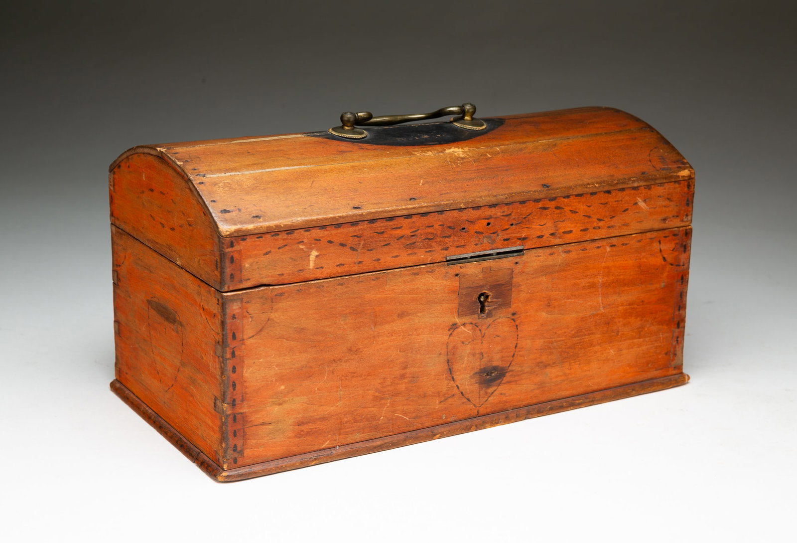 ENGLISH PAINT-DECORATED PINE DOME TOP BOX.: English, ca. 1800. Pine. Box with dovetailed construction, staple hinges, all over red paint with painted flower, hearts and line decoration. Brass bail handle to top. 6"h. 11.75"w. 6"d.Provenance: Fr