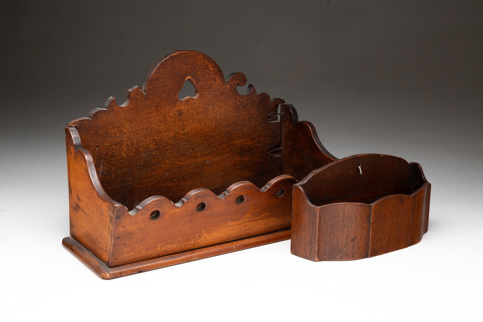 TWO AMERICAN WALL BOXES.: American, 20th Century. Walnut and wood. Shaped back with scrolls, shaped sides, scalloped and pierced front. 8"h.13"w. 4.75"d. Arched back, shaped sides, paneled serpentine front. 4"h. 7.5"w. 2.5"d.P