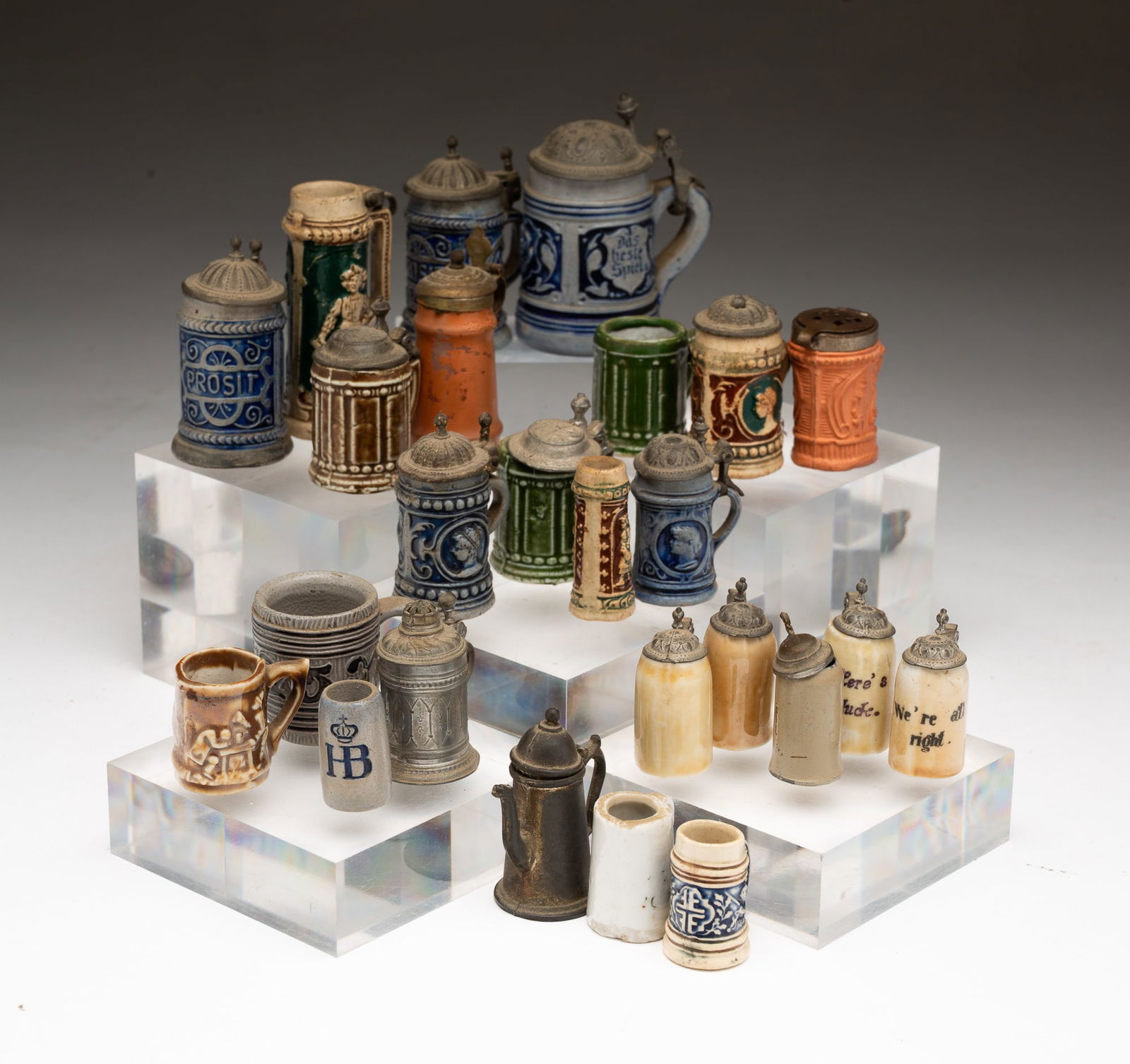TWENTY-FIVE MINIATURE STONEWARE STEINS.: American, 19th and 20th Centuries. Various designs, sizes, and makers, most with lids. Tallest, 2.75"h.Provenance: From the Lifetime Collection of the late Joanne & David Hill (Arcanum, Ohio).