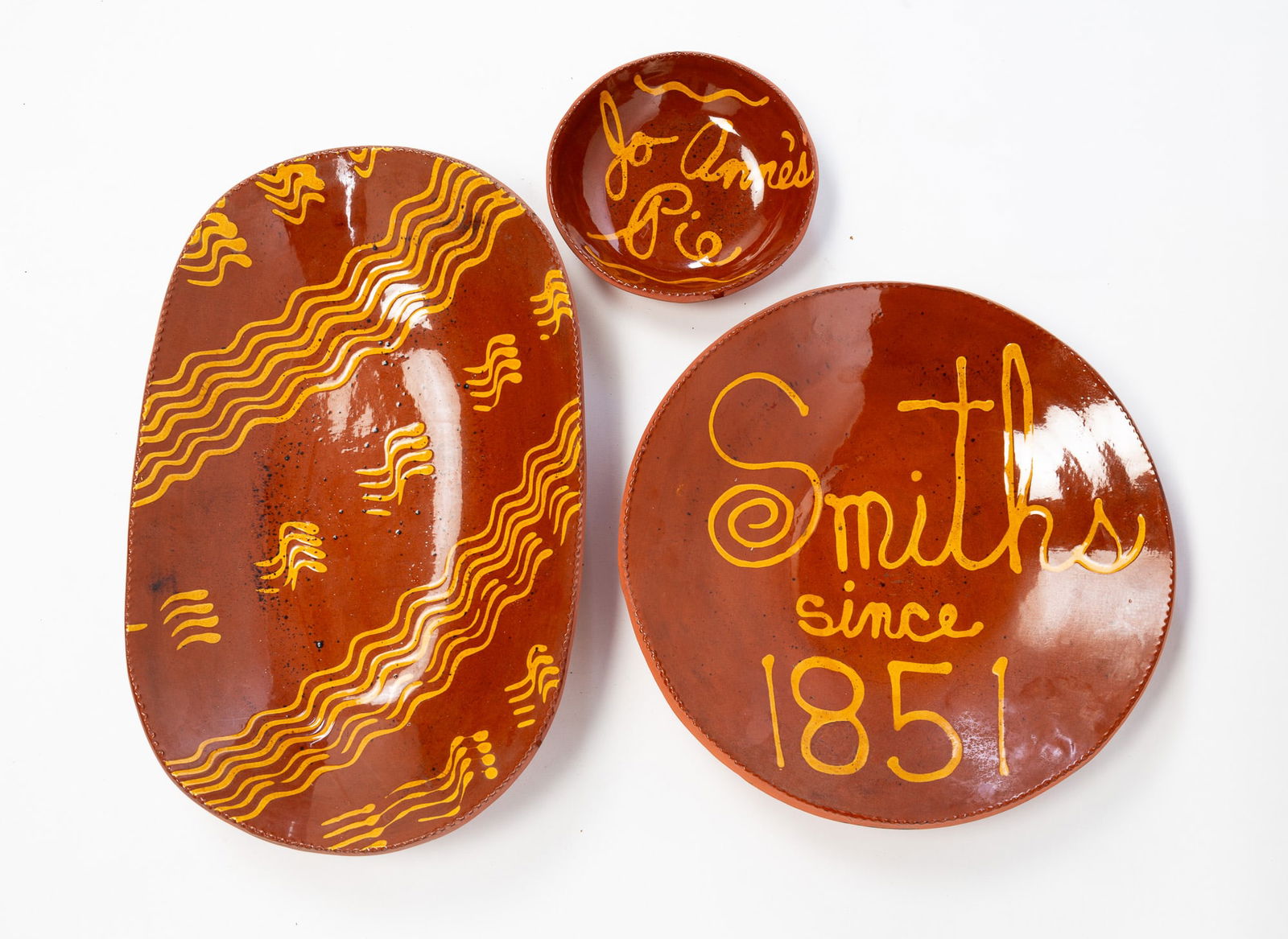 THREE LESTER BREININGER JR. (ROBESONIA, PENNSYLVANIA, 1935-2011) SLIP-DECORATED REDWARE DISHES.: Lester Breininger Jr. (Robesonia, Pennsylvania, 1935-2011), 20th Century. All have coggled rims, an orange and black mottled glaze, and yellow slip decoration. Large oval platter and yellow slip squig