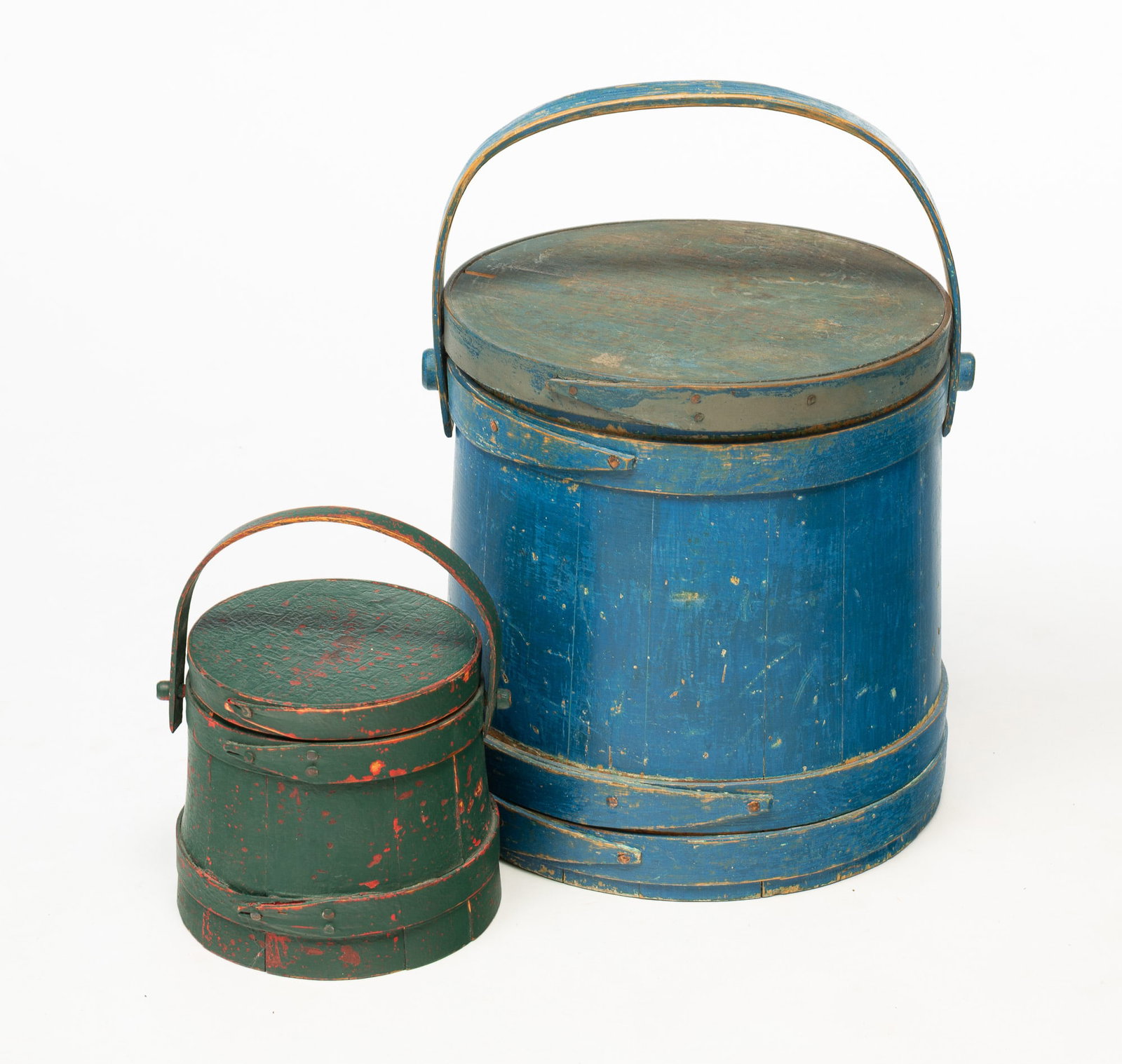 TWO AMERICAN PAINTED FIRKINS.: American, 19th Century. Stave construction with tacked lapped bands and bentwood swing handles. Largest with worn blue paint, 12.75"h. The smaller with tacked bands, bentwood swing handle and green ov