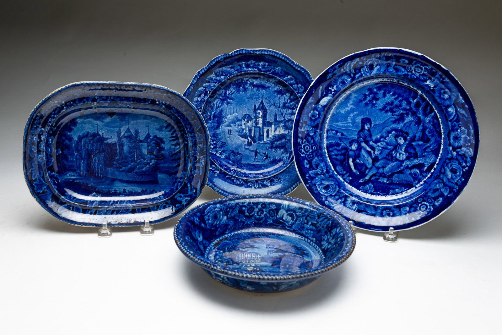 FOUR BLUE TRANSFERWARE STAFFORDSHIRE DISHES.: English and American, 19th Century. Comprising a Clews oval plate of "Eastview of LaGrange The Residence of the Marquis LaFayette," an unmarked round plate of an estate with figures, an E&G Phillips L