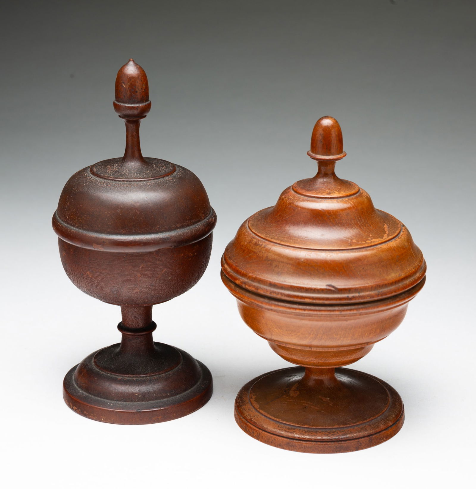 TWO TREENWARE LIDDED AND FOOTED JARS.: American, 19th Century. Turned wood jar having a lid with acorn finial and ring at rim, a bulbous body, and raised on a ringed pedestal foot, with dark alligatored finish. 7.25"h. 3.25"d. Turned wood