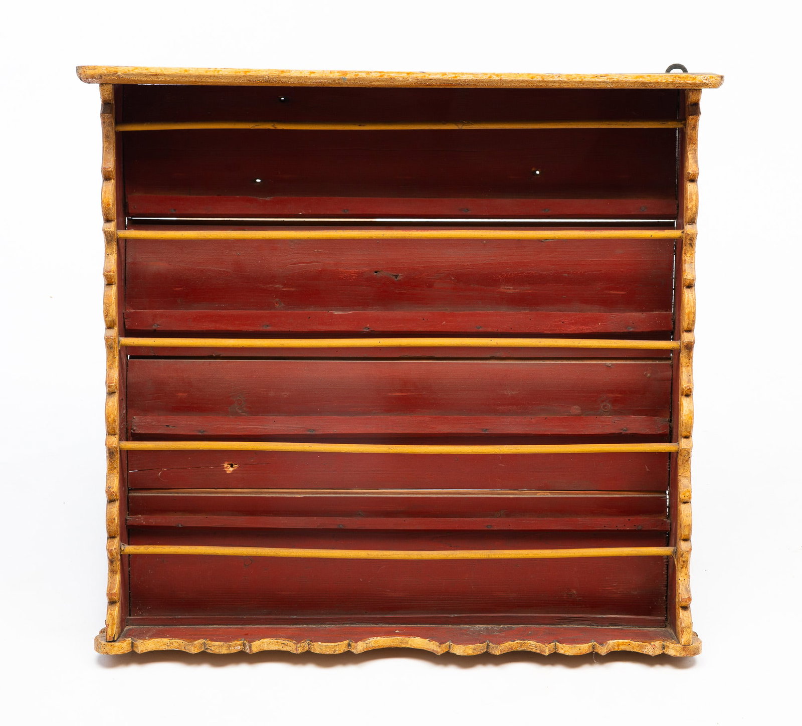 AMERICAN PAINT-DECORATED HANGING PLATE RACK.: American, Late 19th Century. Flat rounded edge top, frame with plate grooves and rails, shaped bottom and sides and decorated with yellow and red paint. 28"h. 29.5"w. 6.5"d.Provenance: From the Lifeti
