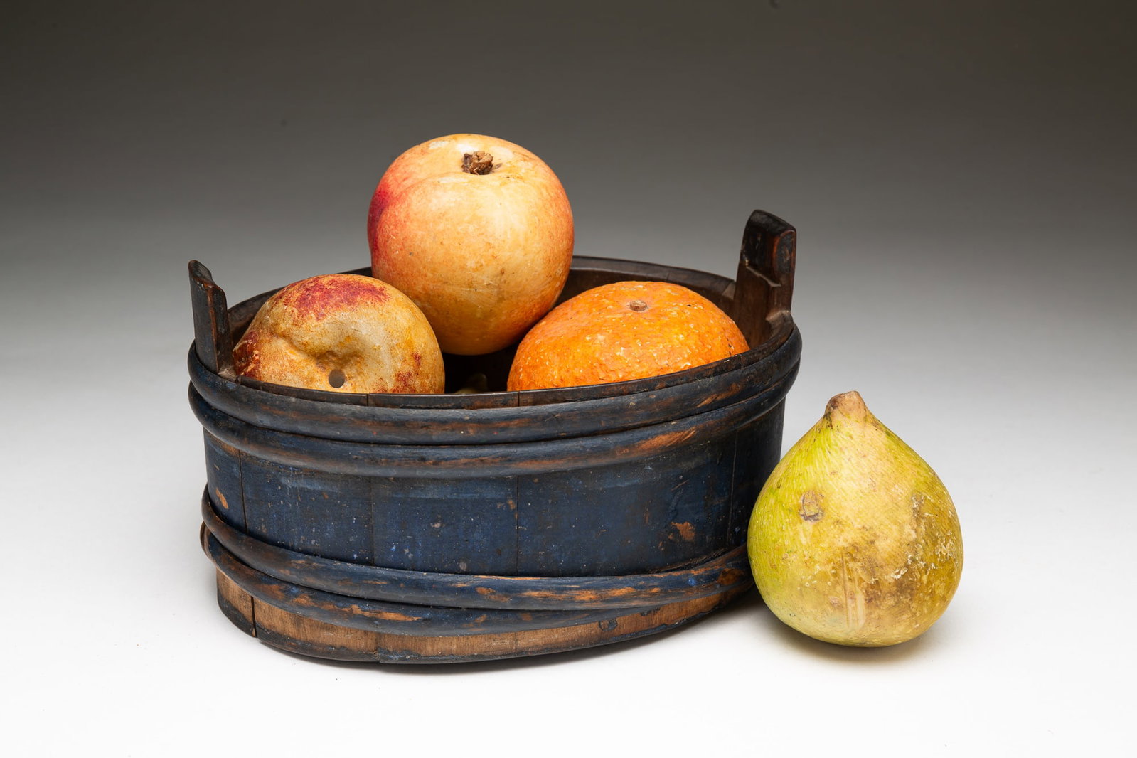 DIMINUTIVE AMERICAN BLUE-PAINTED AND STAVED TUB WITH STONE FRUIT.: American, 19th-20th Century. Oval from tub with two handles and lapped stave construction. 4.5"h. 8.5"w. 6.25"d. Five stone fruits, comprising an apple, a pear, a peach, an orange, and a banana. Six i