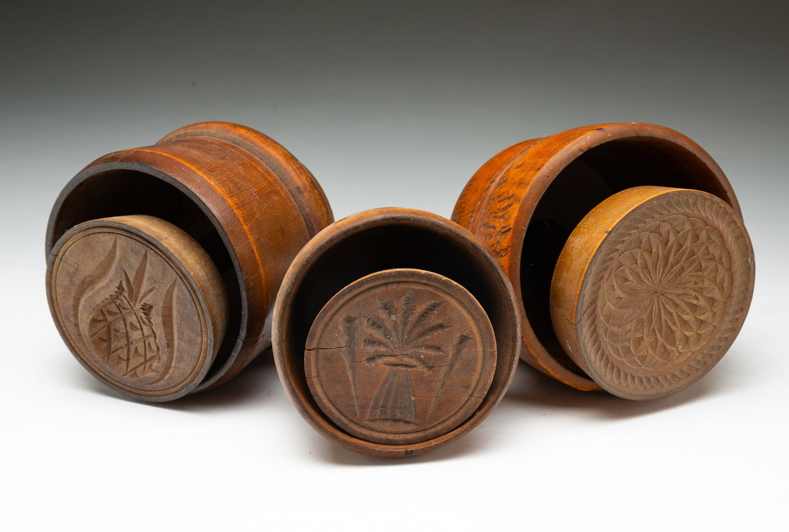THREE AMERICAN WOODEN CASED BUTTER MOLDS.: American, 19th Century. In three carved designs, comprising a geometric floral motif, a teasel, and a sheaf of wheat. Largest, 5"h. 4.75"d.Provenance: From the Lifetime Collection of the late Joanne &