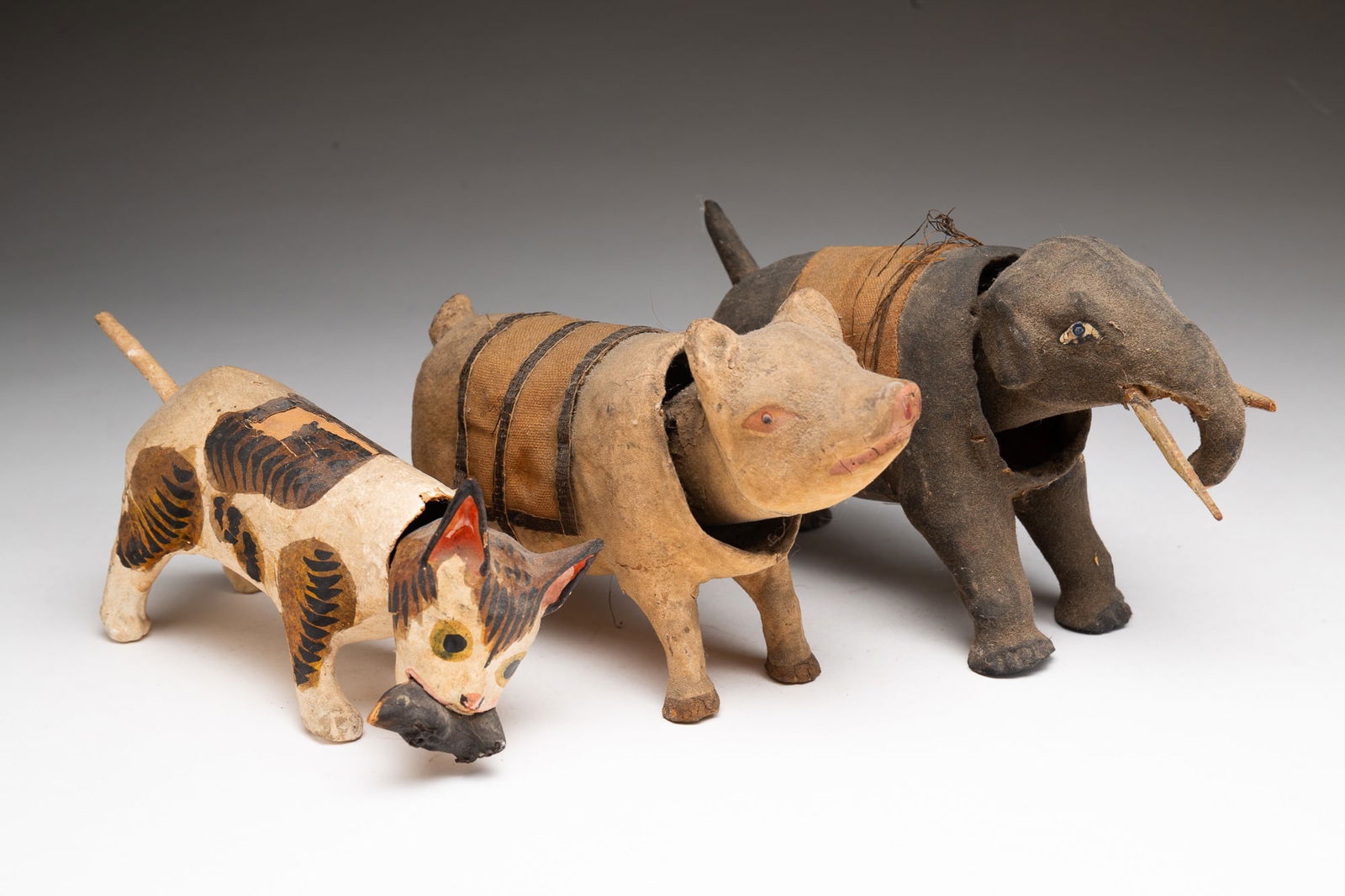 THREE GERMAN PAPIER-MACHE NODDING CAT, ELEPHANT, AND PIG FIGURINES.: Germany, ca. 1900. Papier-mache. Comprising a white and black-brown striped cat holding a black mouse in its mouth, a gray elephant with a linen saddle blanket, and a tan pig with a linen and leather
