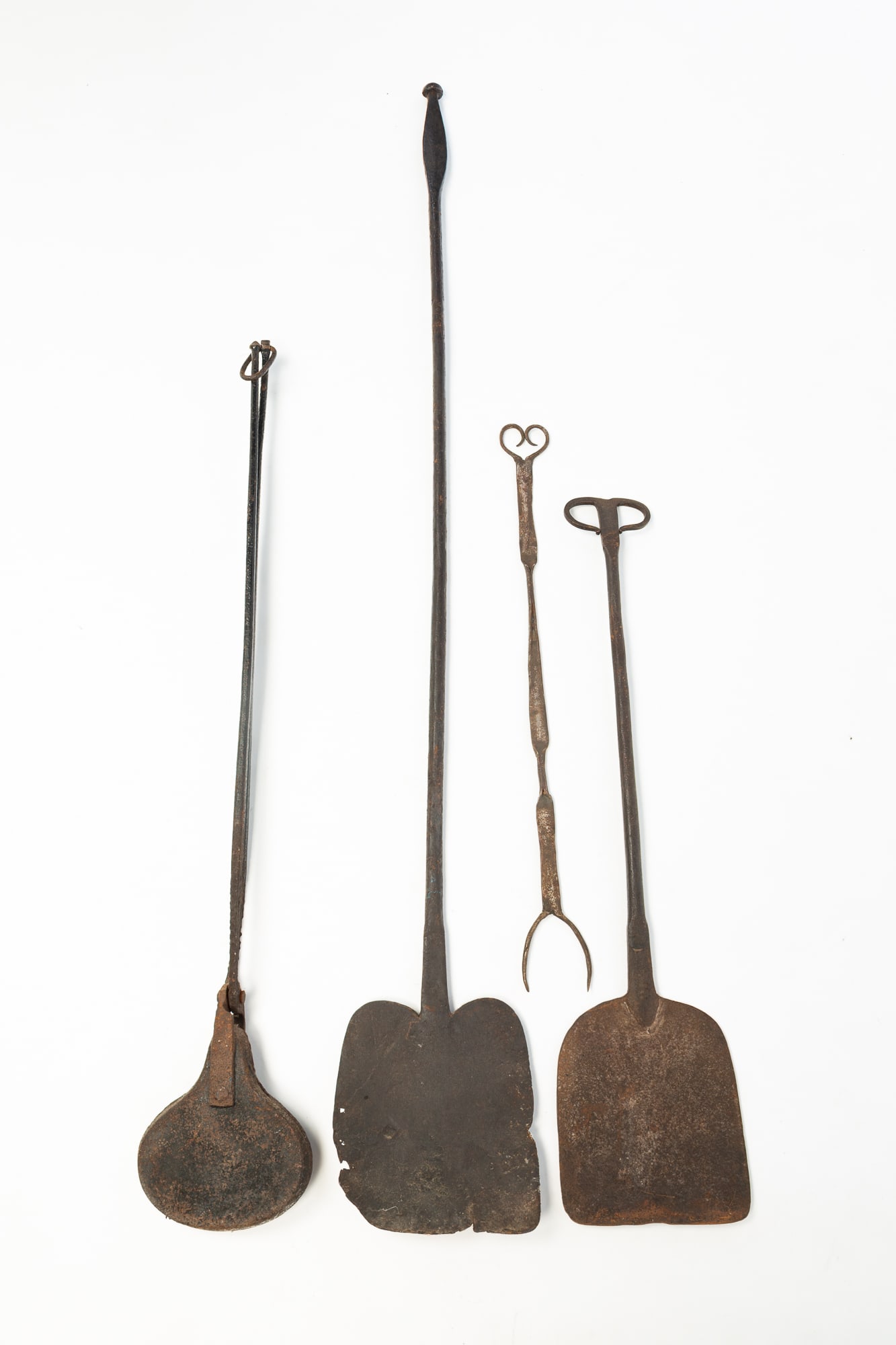 GROUP OF FORGED IRON HEARTHSIDE ACCESSORIES.: America, 19th Century. Forged iron. Includes two peels, one with rams head handle, a waffle iron and a two tine form with heart handle. From 50"l. to 24"l.Provenance: From the Lifetime Collection of t